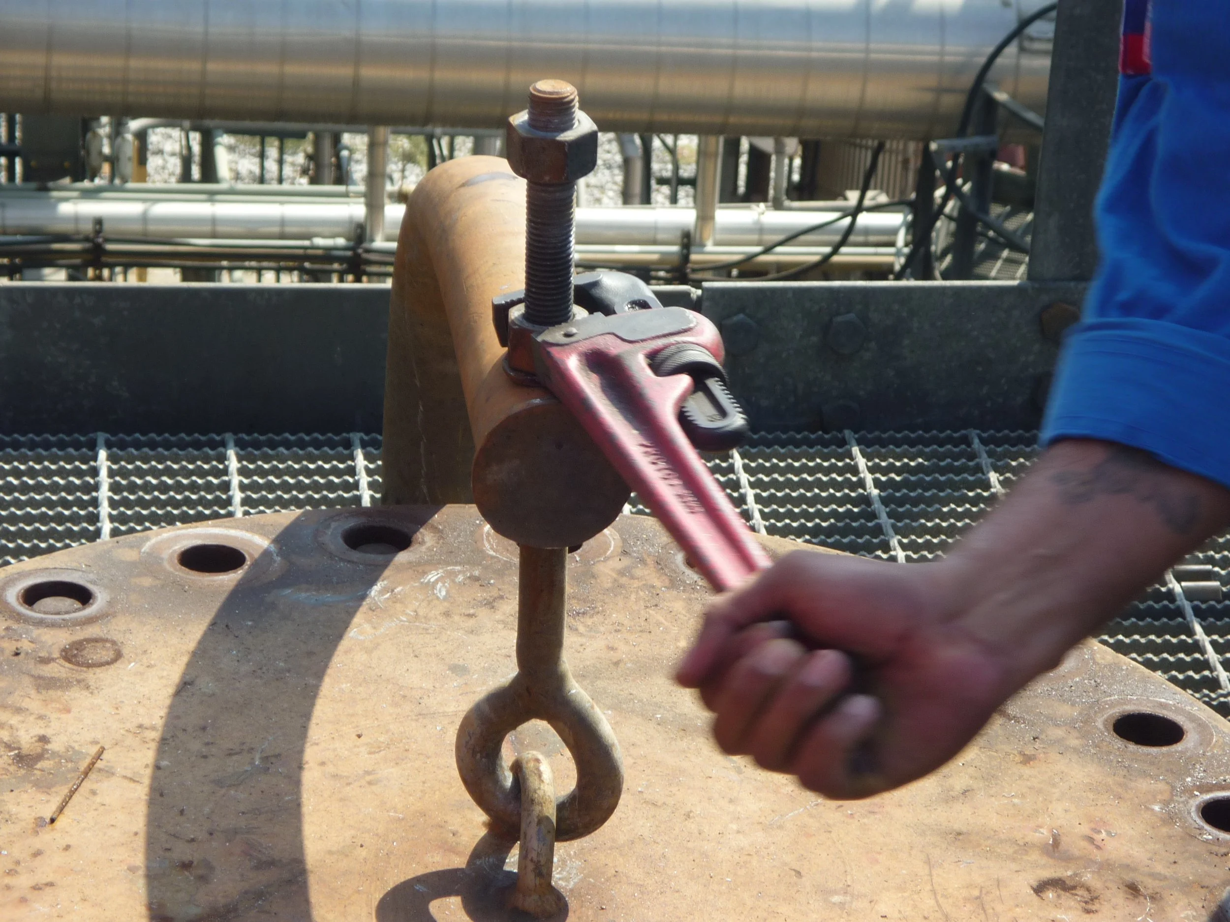 Persona ajustando una tuerca grande con una herramienta en una estructura metálica en una planta industrial.