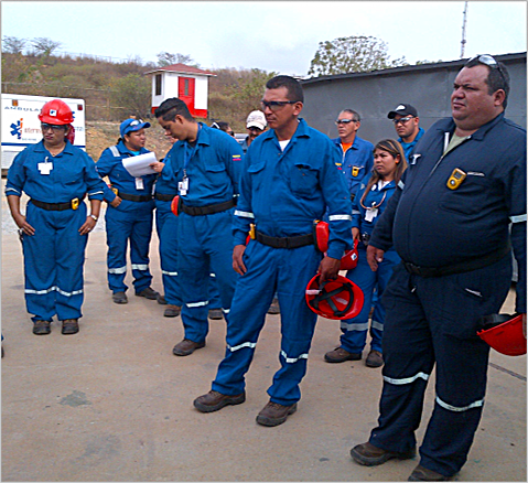 Simulacro de Seguridad industrial. Grupo de personas vestidas con uniformes azules y algunos con cascos y gafas de protección en un ambiente al aire libre.