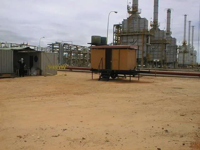 Escenario en una planta industrial con estructuras de metal, una pequeña estructura móvil en el centro y una persona en la esquina izquierda.