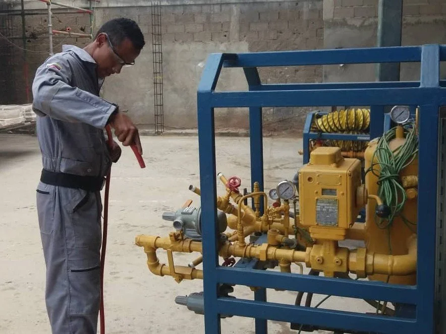 Un hombre con gafas trabaja en una máquina de electricidad en un espacio en construcción con paredes de ladrillo y cemento.