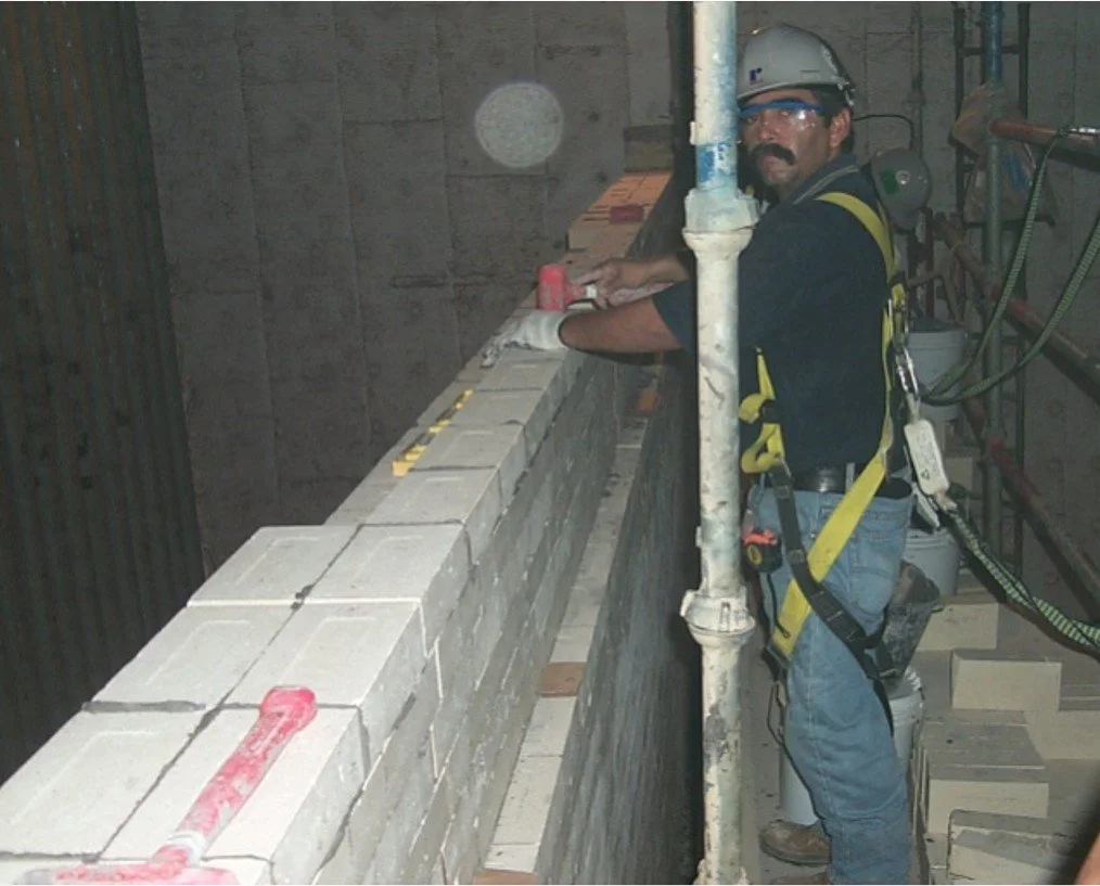 Un trabajador de construcción usando casco y arnés, colocando ladrillos refractario en un muro.