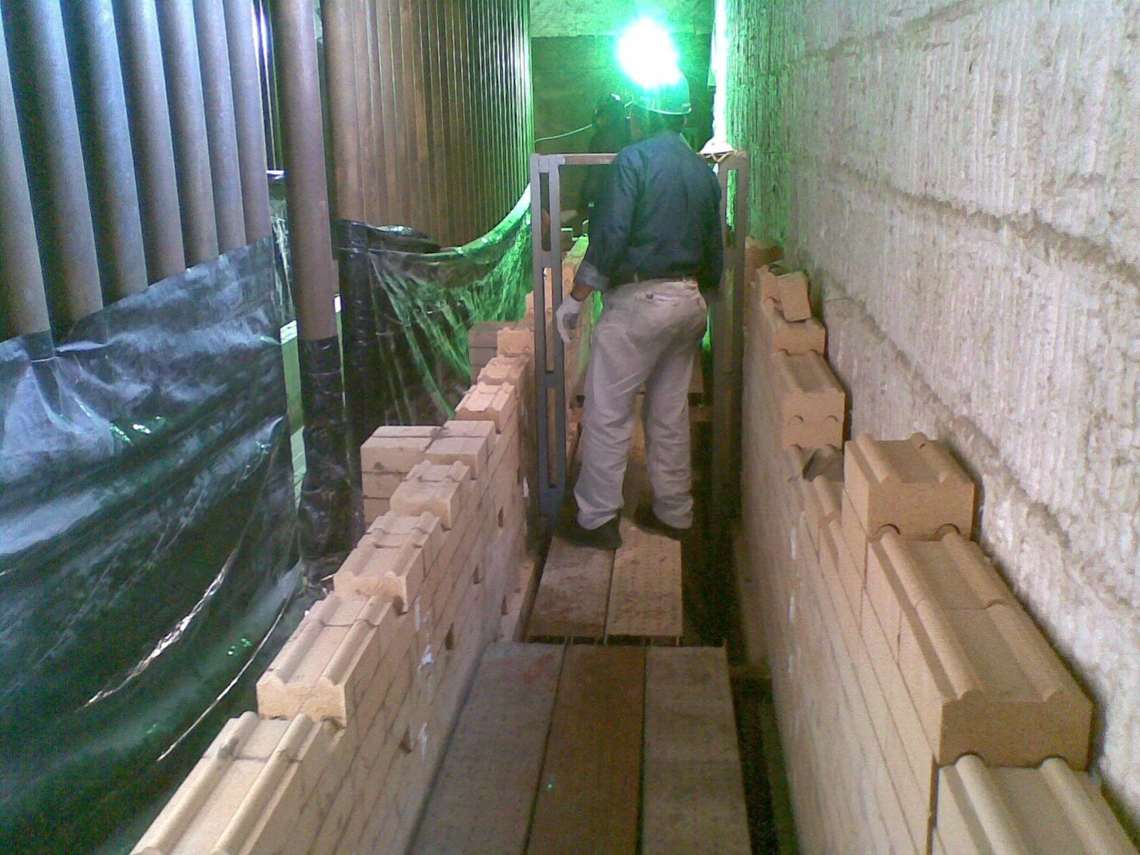 Trabajador en un pasillo con paredes de ladrillos, colocando ladrillos refractarios en una línea, con equipo de protección 
