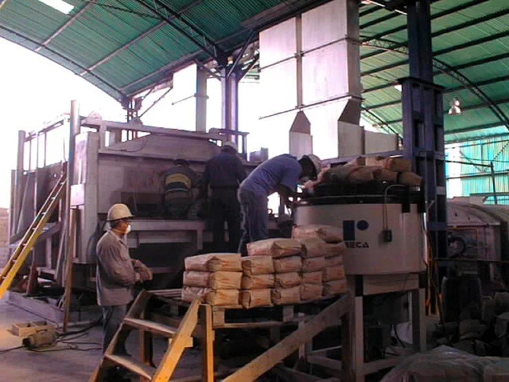 Personas operando mezcladora en un horno de fundicion, apilando sacos de cemento.