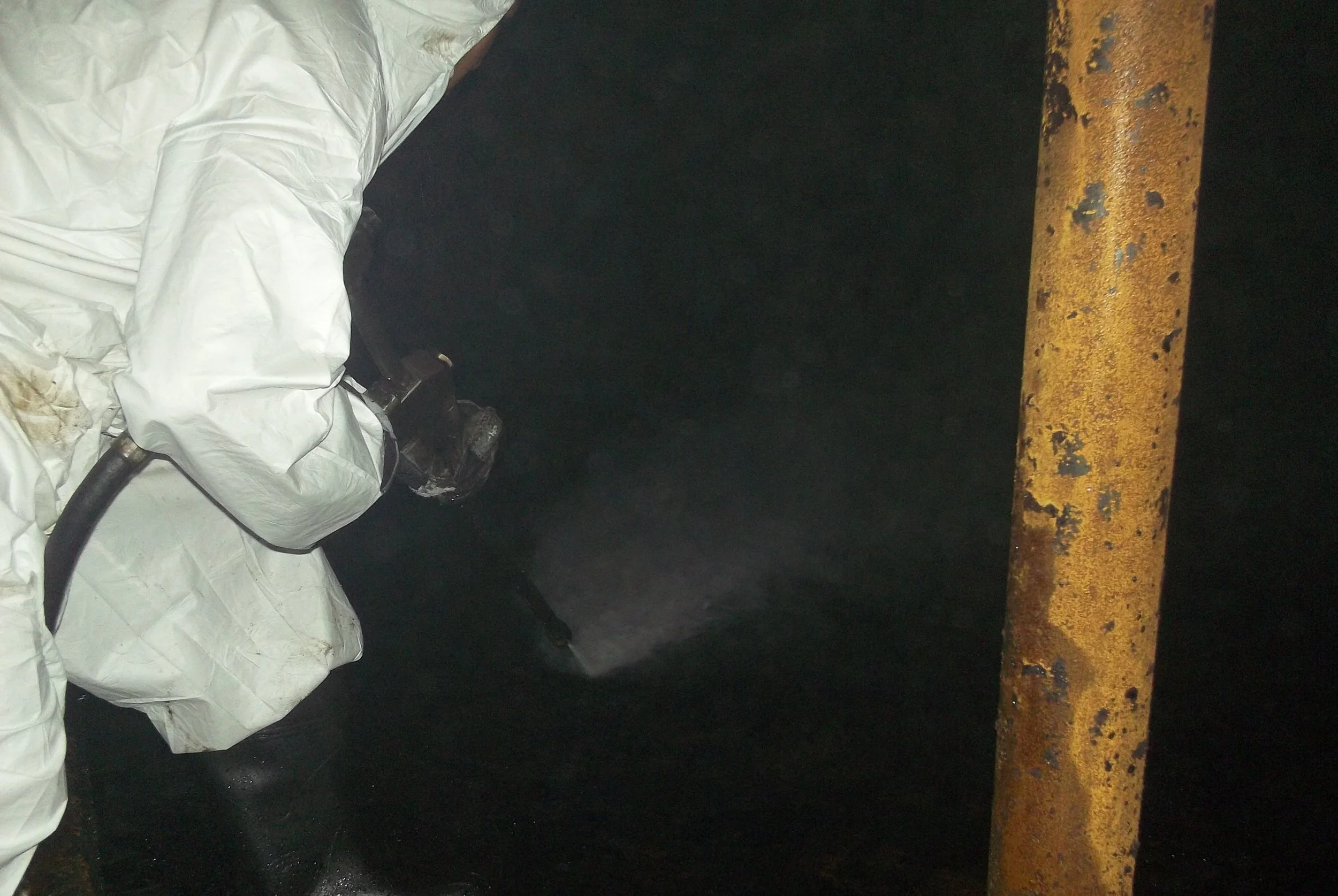 limpieza quimica, Persona rociando un líquido en un área oscura con una tubería amarilla oxidada