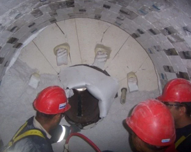 Hormo Clauss.Tres trabajadores con cascos rojos trabajando en la construcción de un horno, observando .