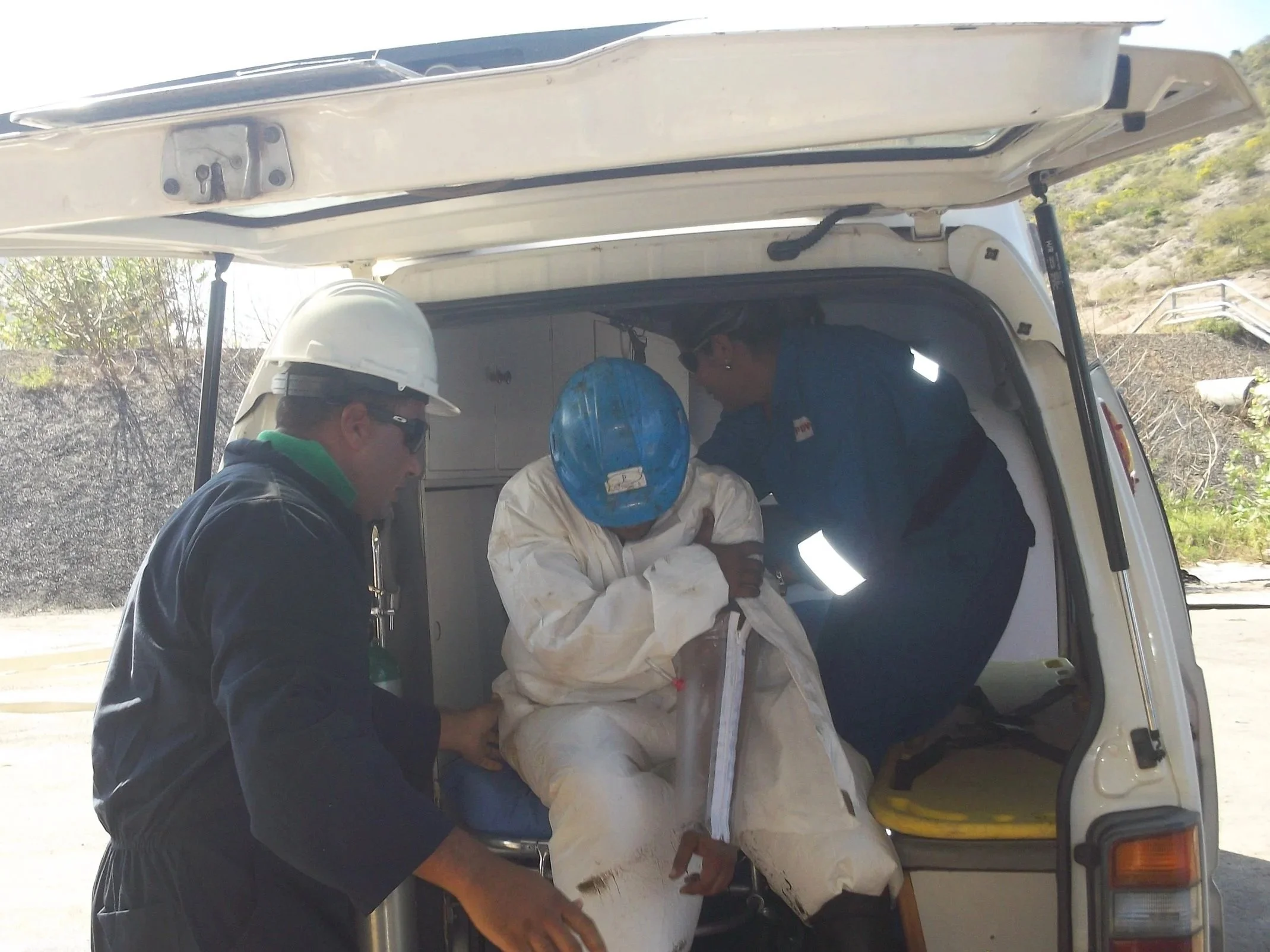 Tres trabajadores con cascos y ropa de protección atendiendo a una persona lesionada en una ambulancia