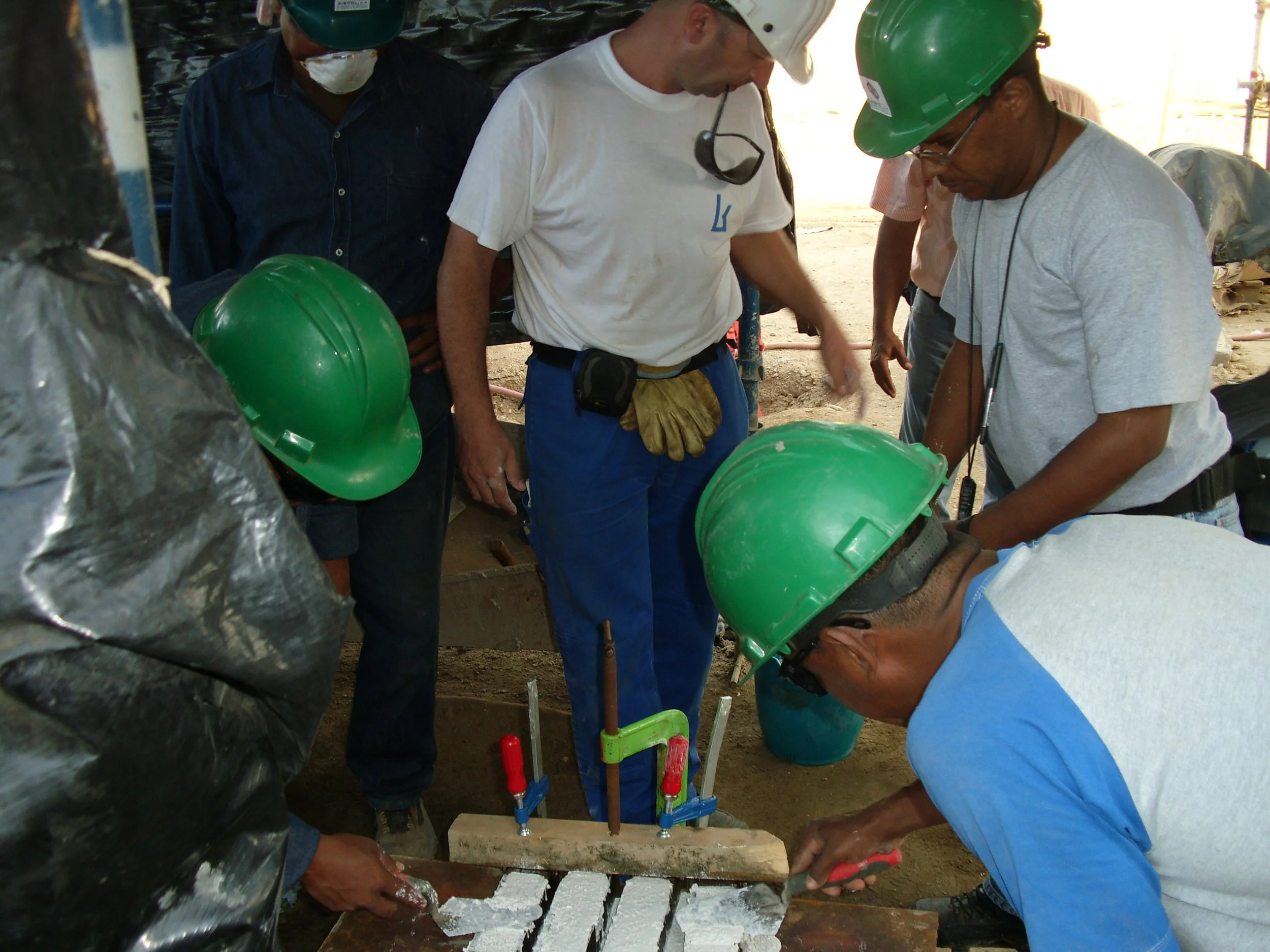 Hombres con cascos verdes y una mujer con casco blanco trabajando en una construcción o obra civil, usando herramientas y equipo de protección, en un ambiente de construcción.