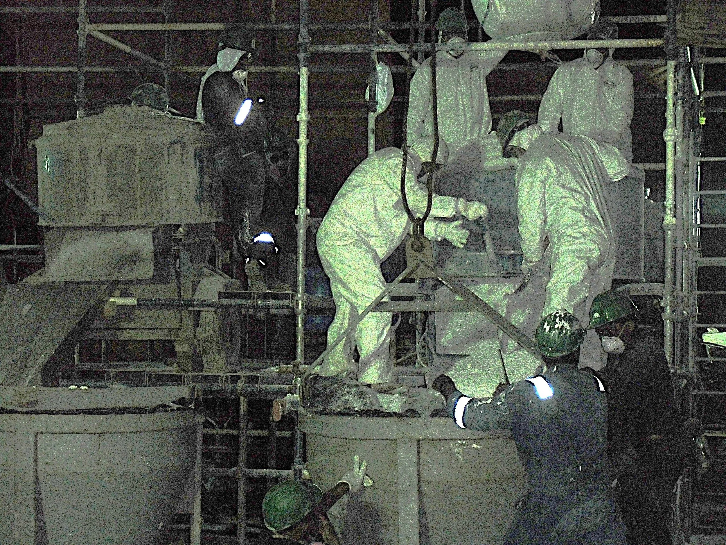 vaciado de reformador secundario. Trabajadores en uniformes y cascos de seguridad mezclando material refractario en una estructura de andamios durante la noche.