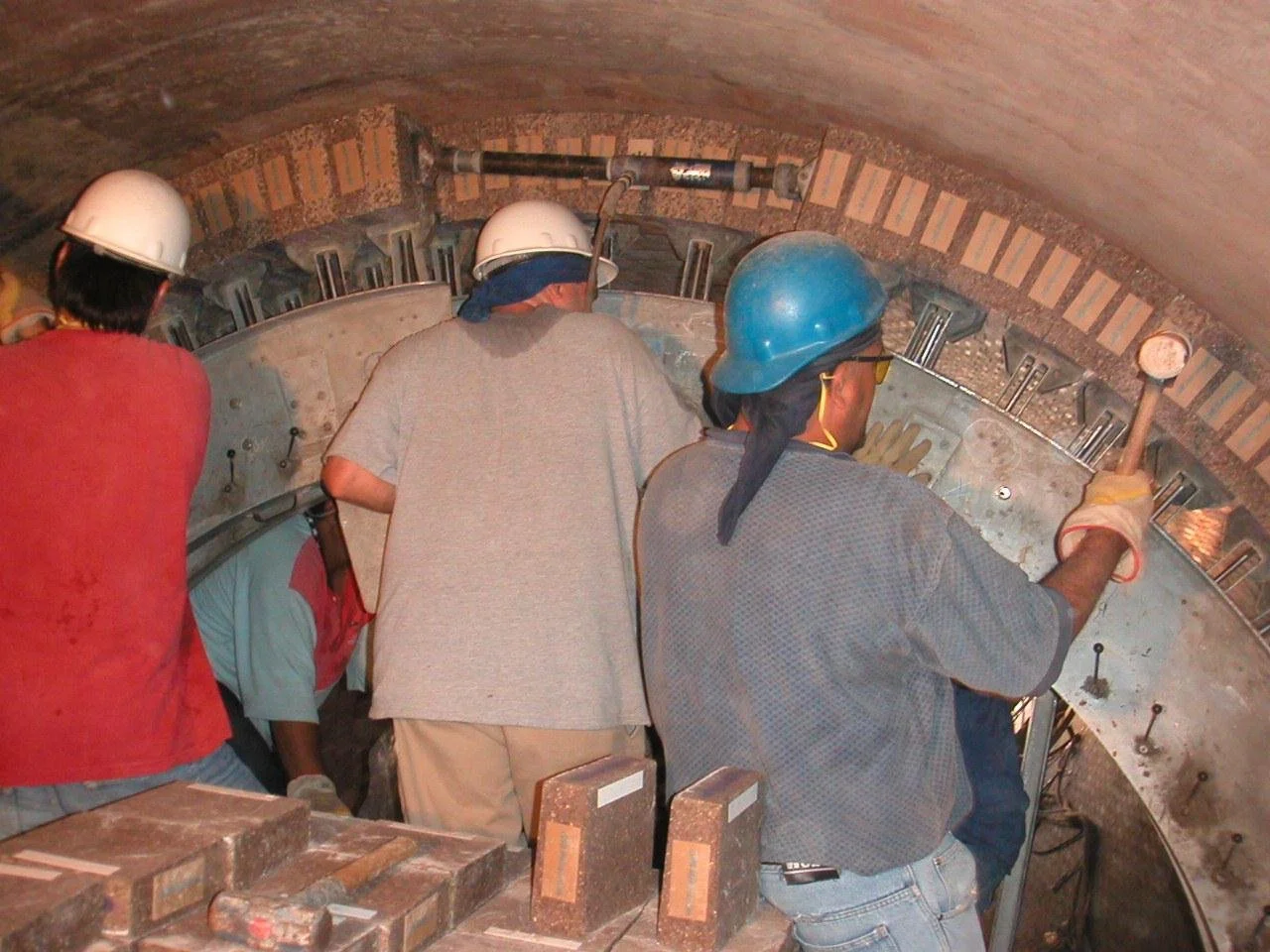 Cuatro trabajadores con cascos de seguridad inspeccionando una estructura de túnel en construcción.