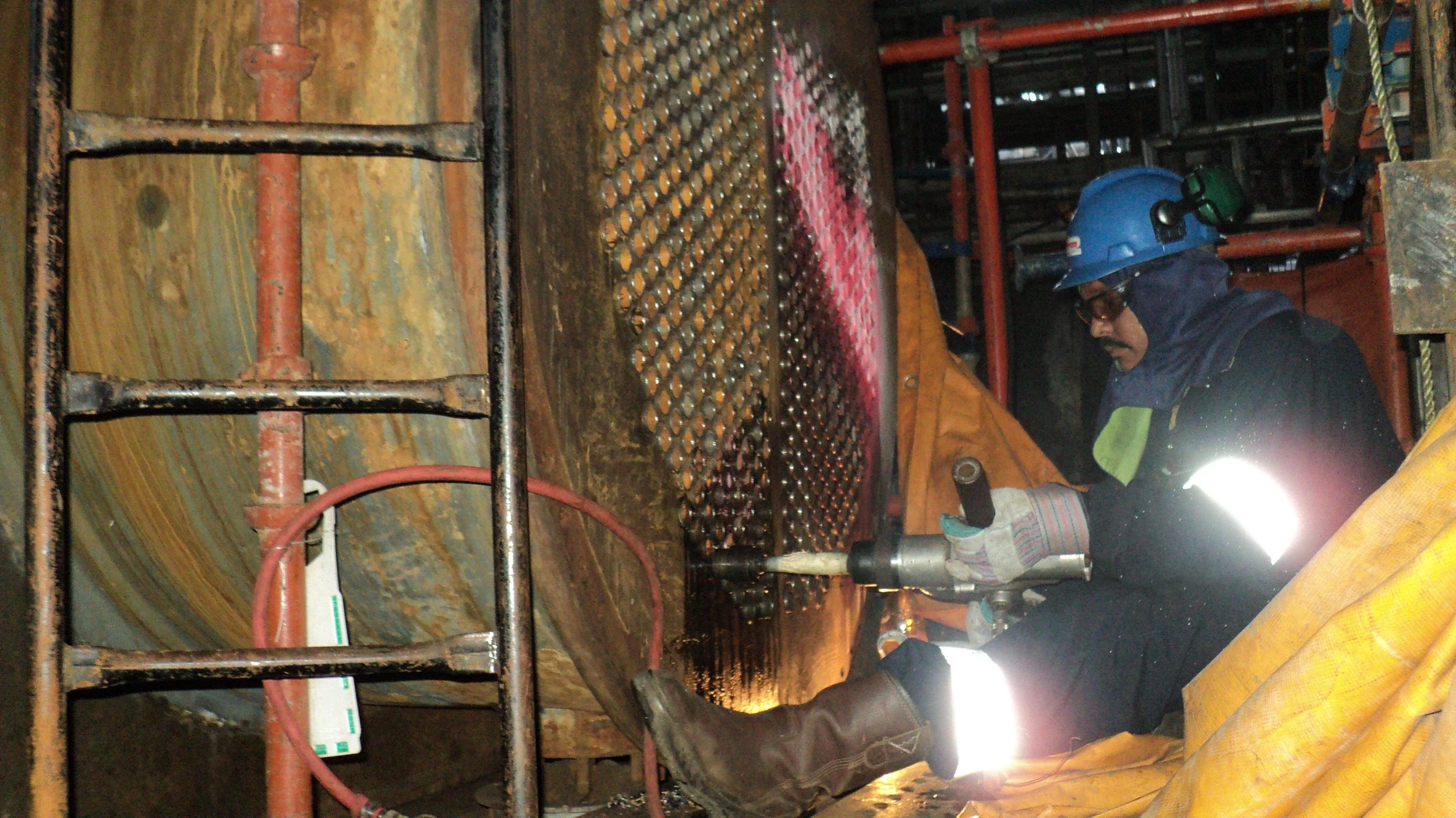 Trabajador de la industria en equipo de protección, usando equipo de seguridad, soldando reentubado intercambiador de calor .