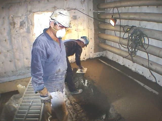 Personas trabajandohaciendo un vaciado en piso en horno, usando herramientas y equipo de protección.