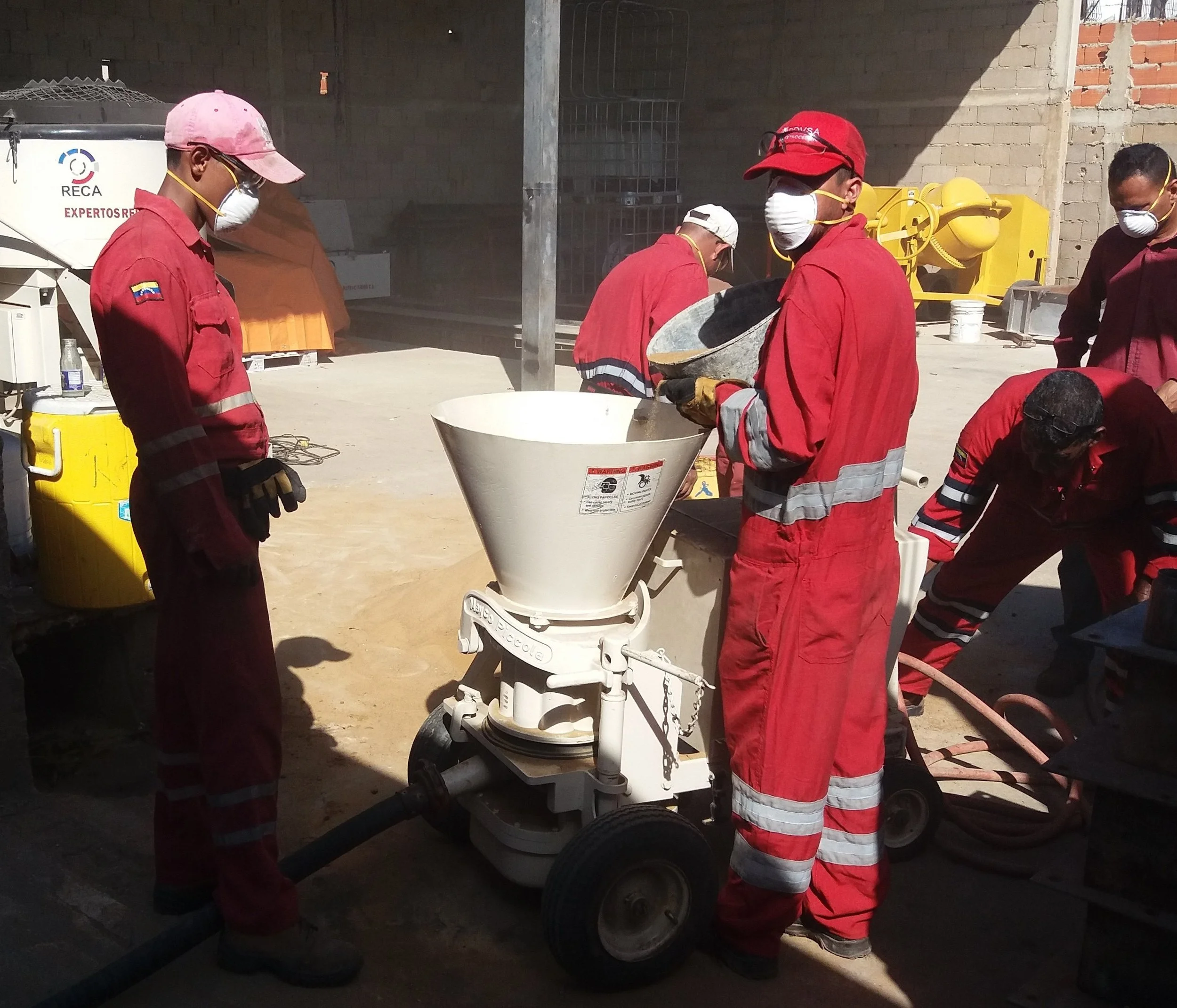 Grupo de trabajadores usando equipo de protección trabajando con una máquina de concreto en un sitio de construcción