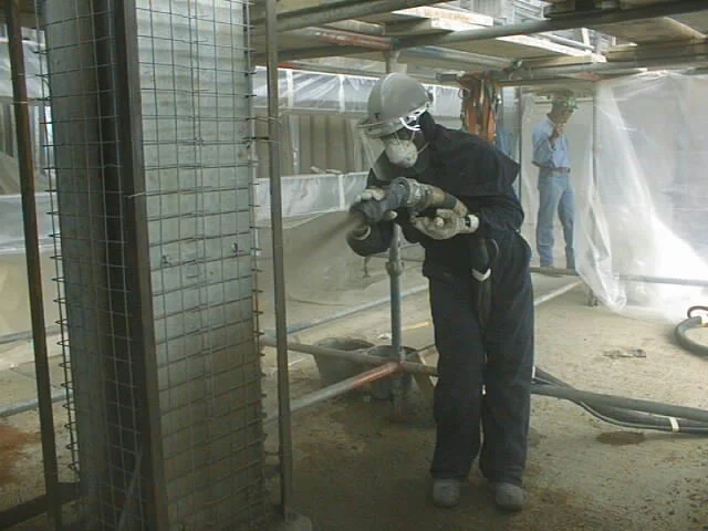 Una persona usando equipo de protección mientras trabaja en una construcción, aparentemente perforando o cortando concreto con una herramienta eléctrica.