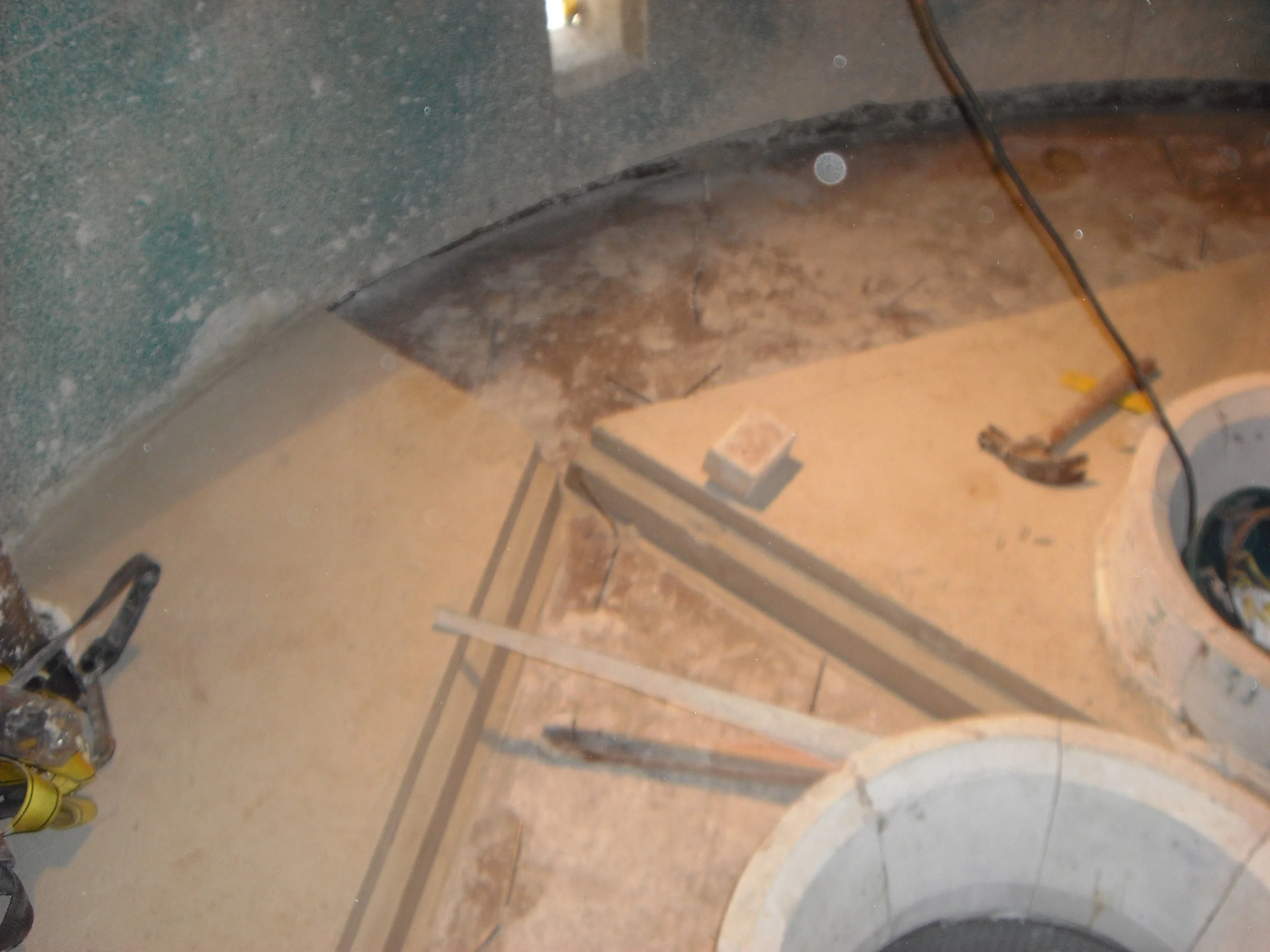 Vista de una construcción en proceso, con paredes de cemento, un borde de granito, tuberías visibles y herramientas de construcción en el suelo.