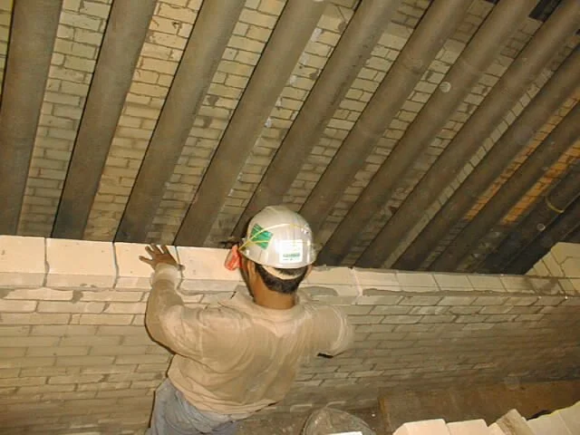 trabajador en pasillo con paredes de ladrillos, colocando ladrillos refractarios  
