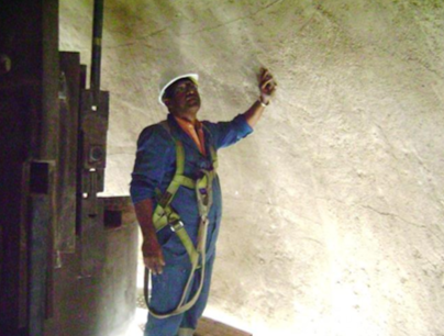 Persona dentro del domo FCC de la refineria , usando equipo de seguridad y señalando la pared.