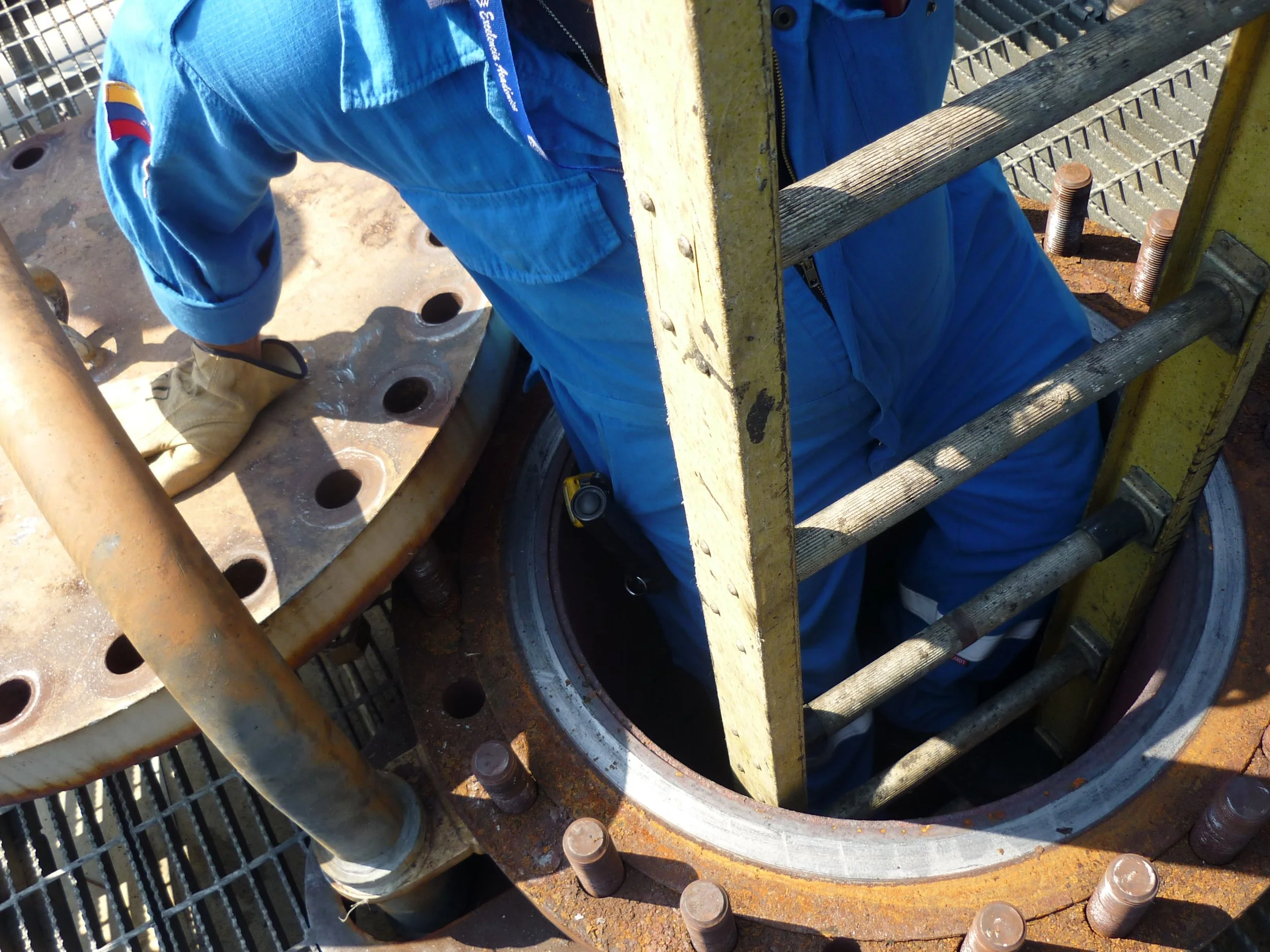 Trabajador en uniforme de trabajo ingresando a una estructura de inspección o mantenimiento en una plataforma industrial o de petróleo.