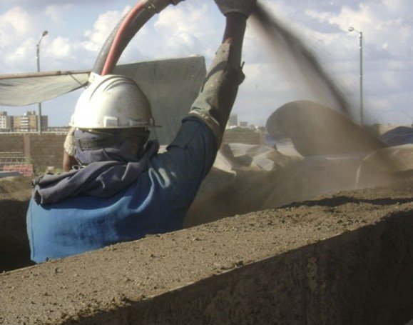 Un trabajador en casco y ropa de protección proyecta material en una construcción.