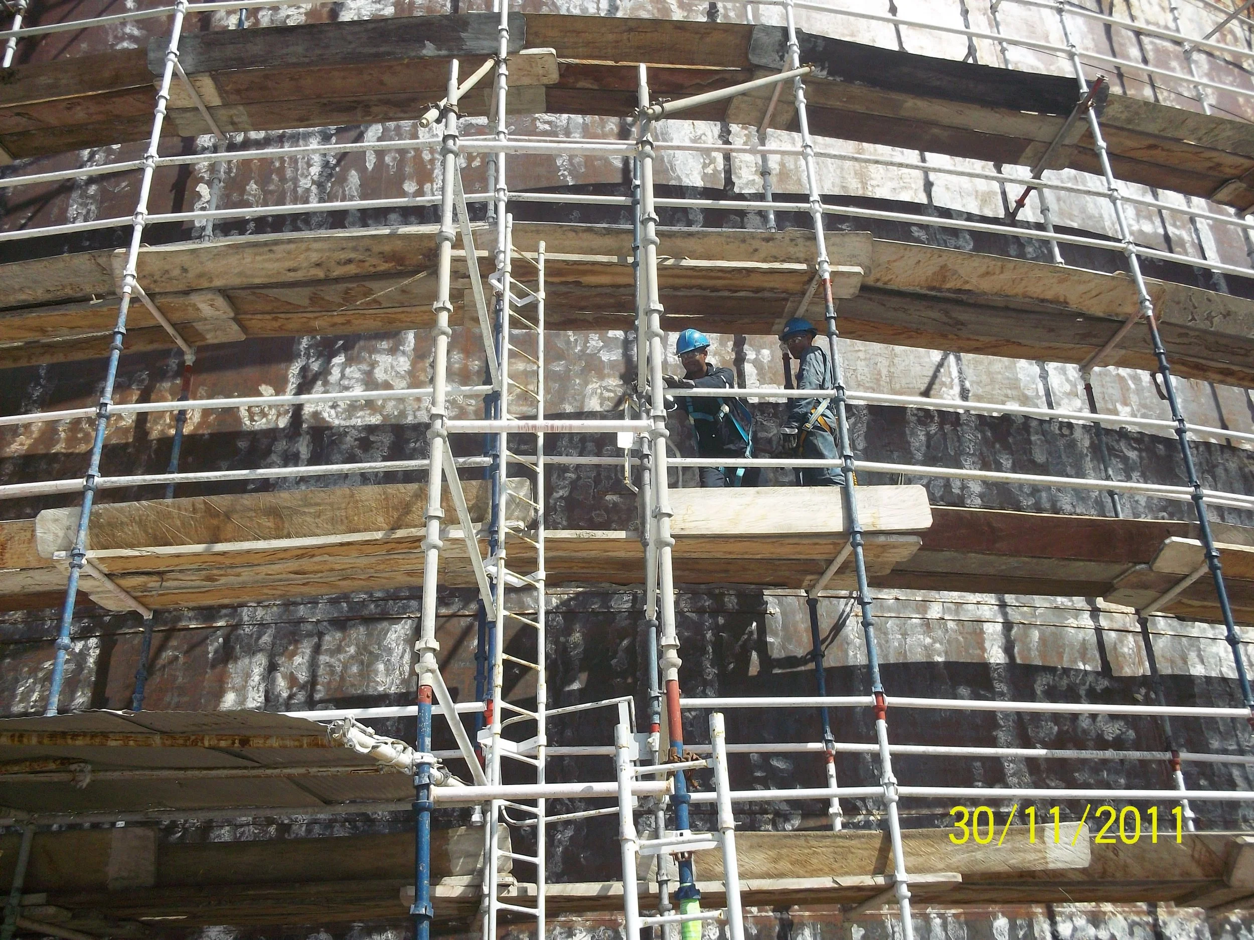 Rehabilitacion. Trabajadores con casco en una estructura de andamios alrededor de tanque de almacenamiento petrolero