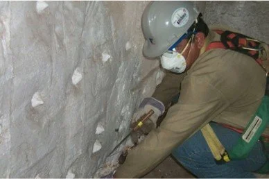 Trabajador en equipo de protección y casco, realizando tareas de excavación en un muro de piedra.