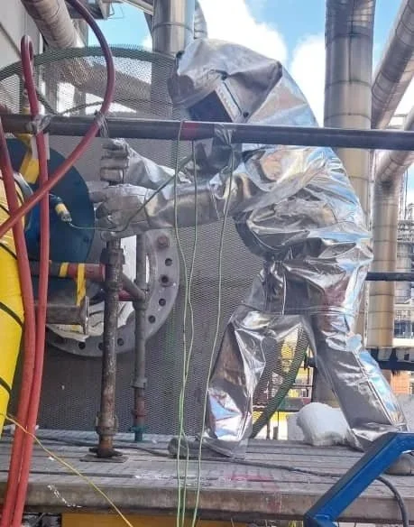 Un trabajador con traje de protección plateado en una maqueta de estructura industrial. Persona con casco en una planta industrial operando equipo portatil de secado dryout