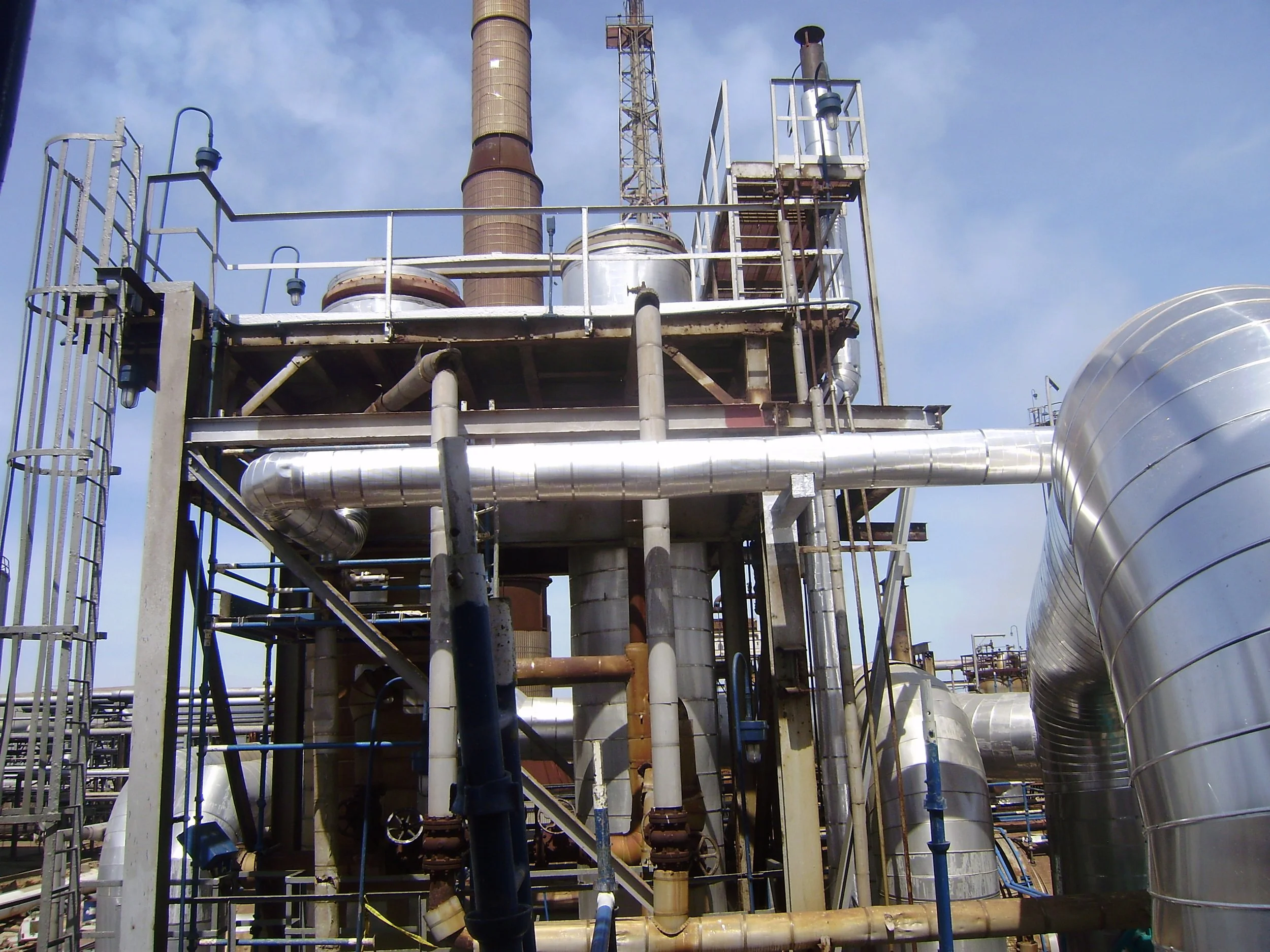 Planta industrial con tuberías de metal y estructura de acero bajo cielo azul.