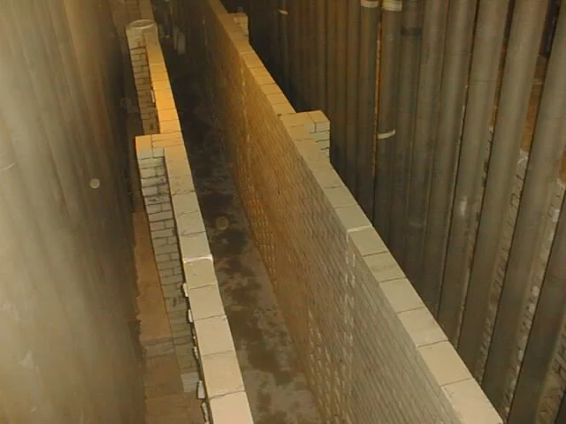 trabajador en pasillo con paredes de ladrillos, colocando ladrillos refractarios  