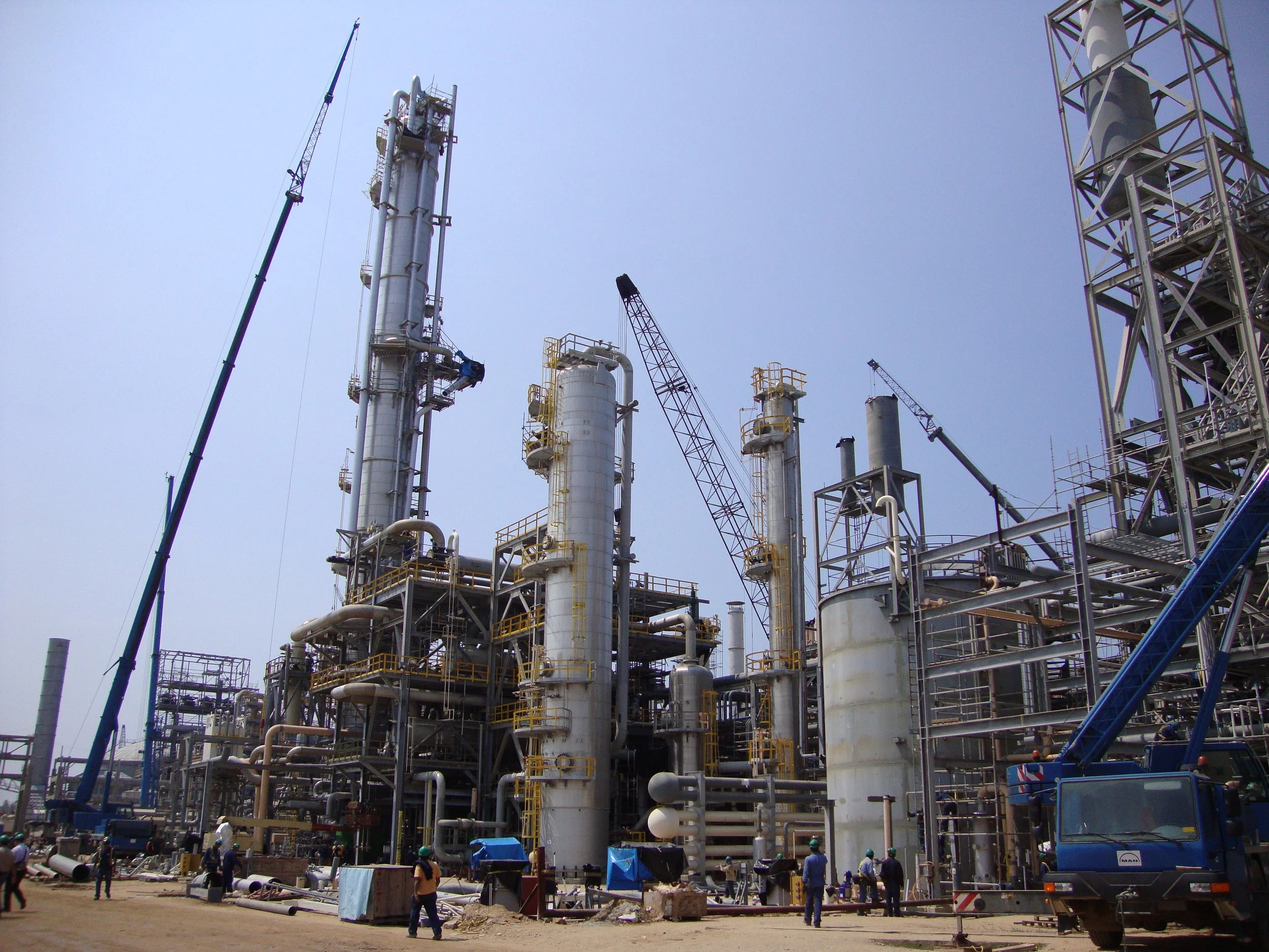 Planta industrial con torres de procesamiento, grúas y trabajadores en el lugar de construcción.