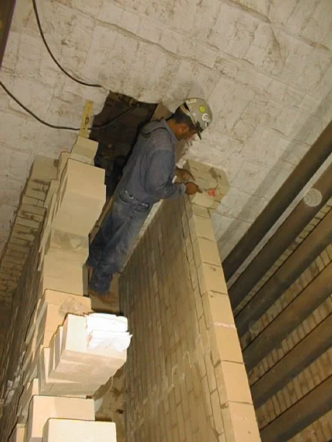 trabajador en pasillo con paredes de ladrillos, colocando ladrillos refractarios  