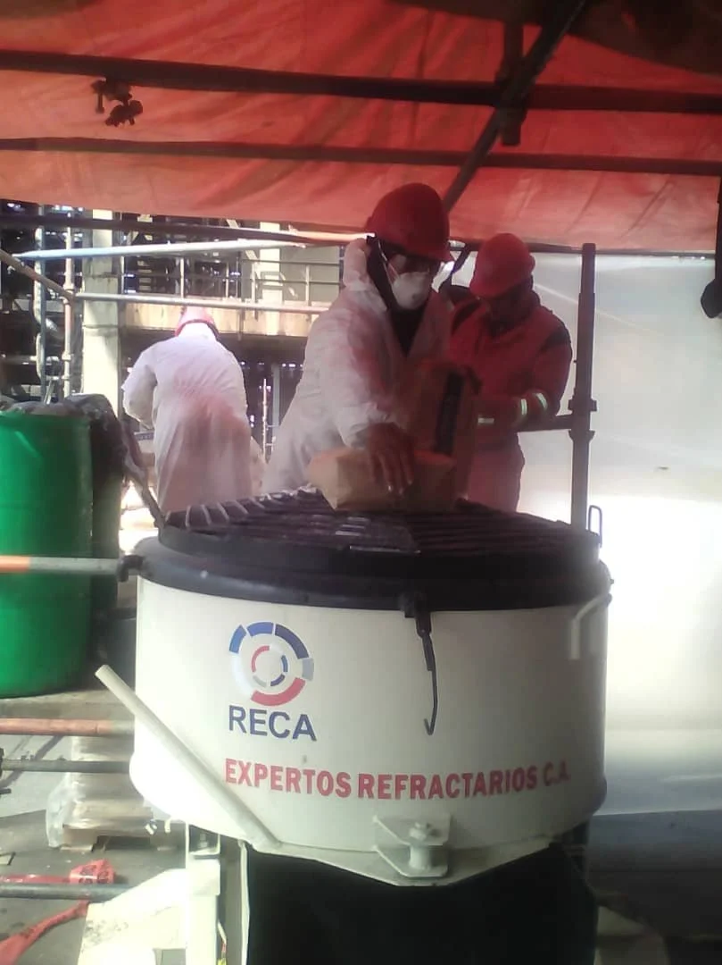 Trabajadores con cascos y mascarillas en una plataforma de construcción, en primer plano hay una mezcladora con el logo RECA y la leyenda 'Expertos refractarios'.