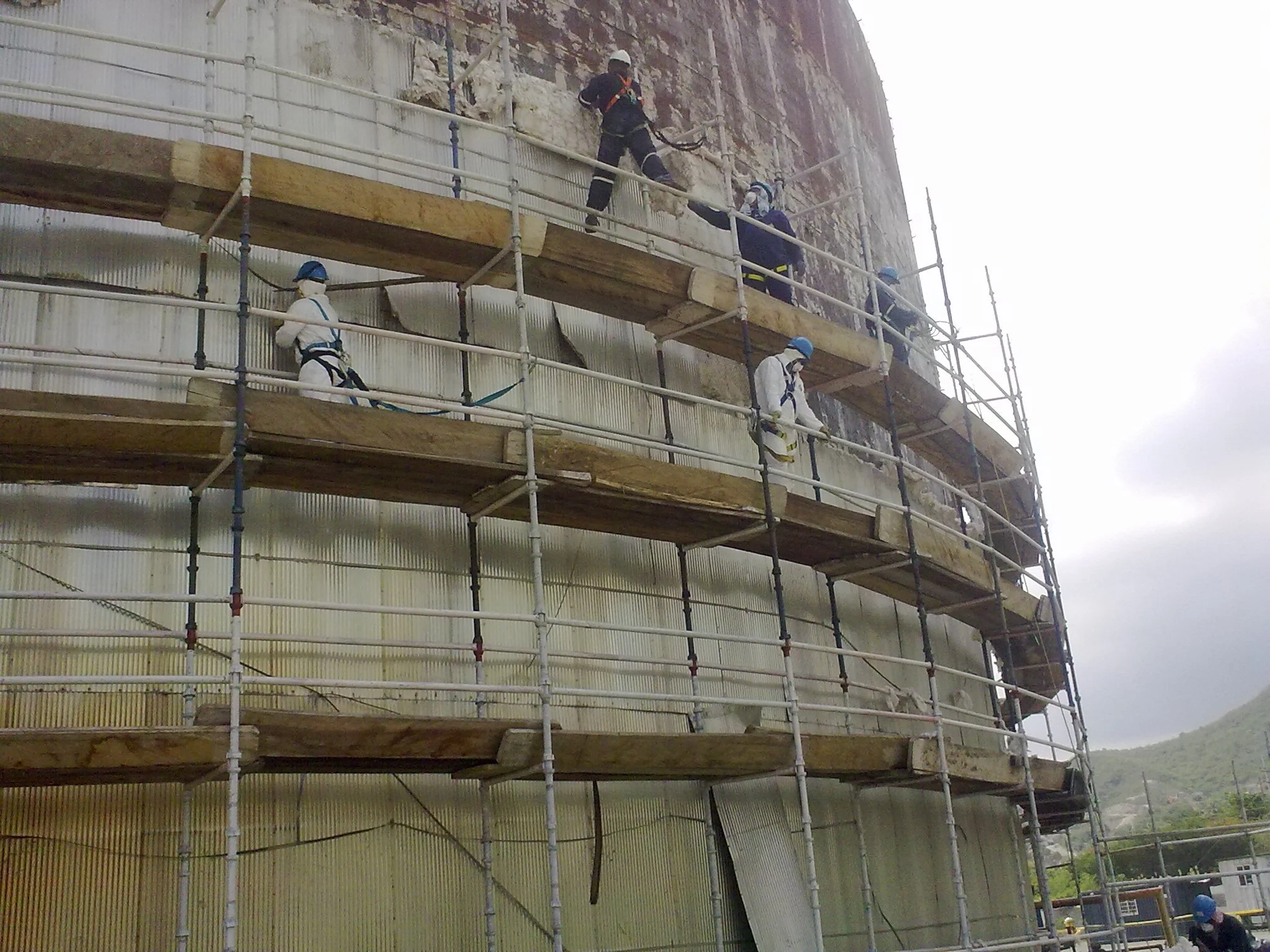 Rehabilitacion. Trabajadores con casco en una estructura de andamios alrededor de tanque de almacenamiento petrolero