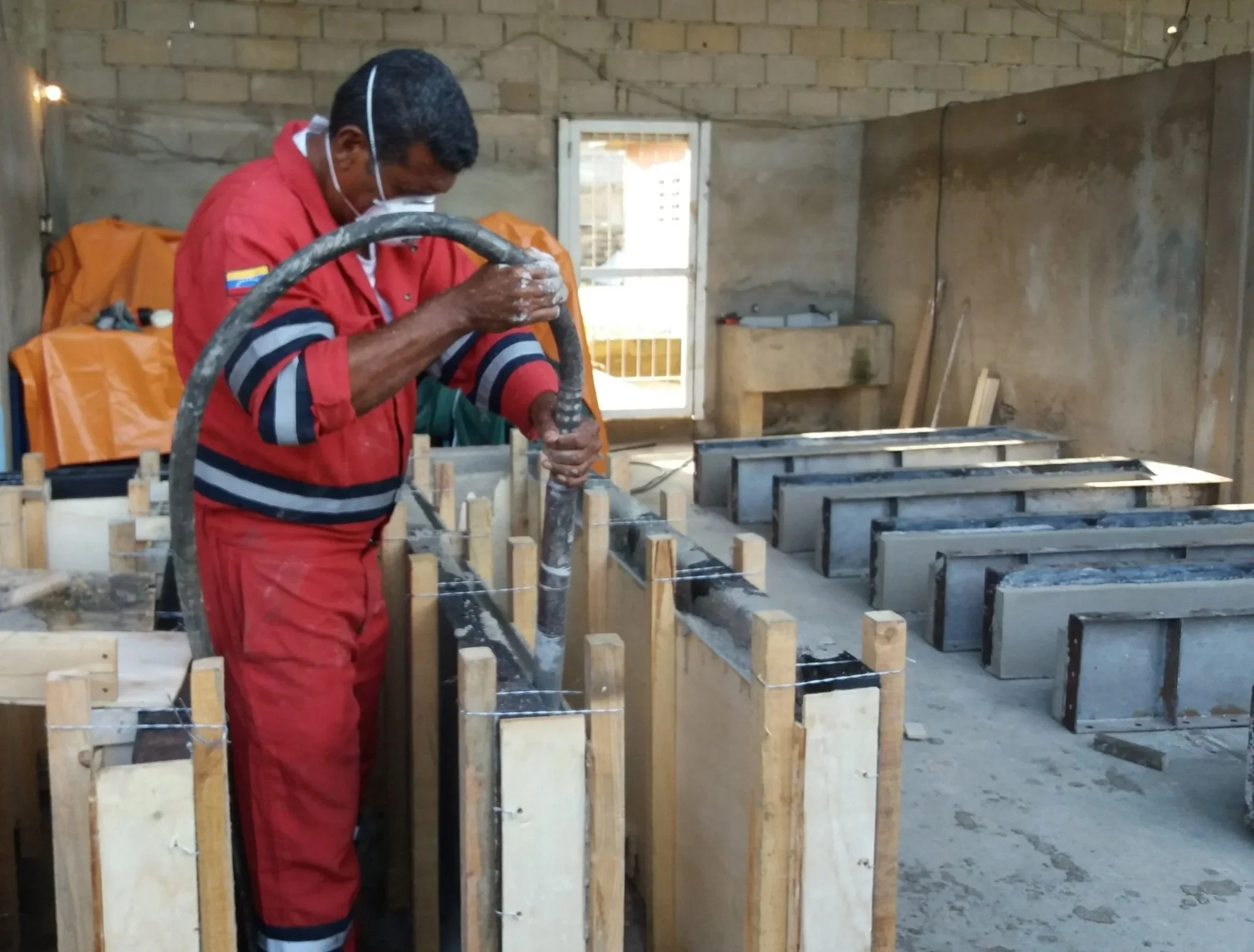 Un hombre trabaja en encofrado metalico de concreto, usando un vibrador de concreto en un encofrado metalico y de madera en un taller.