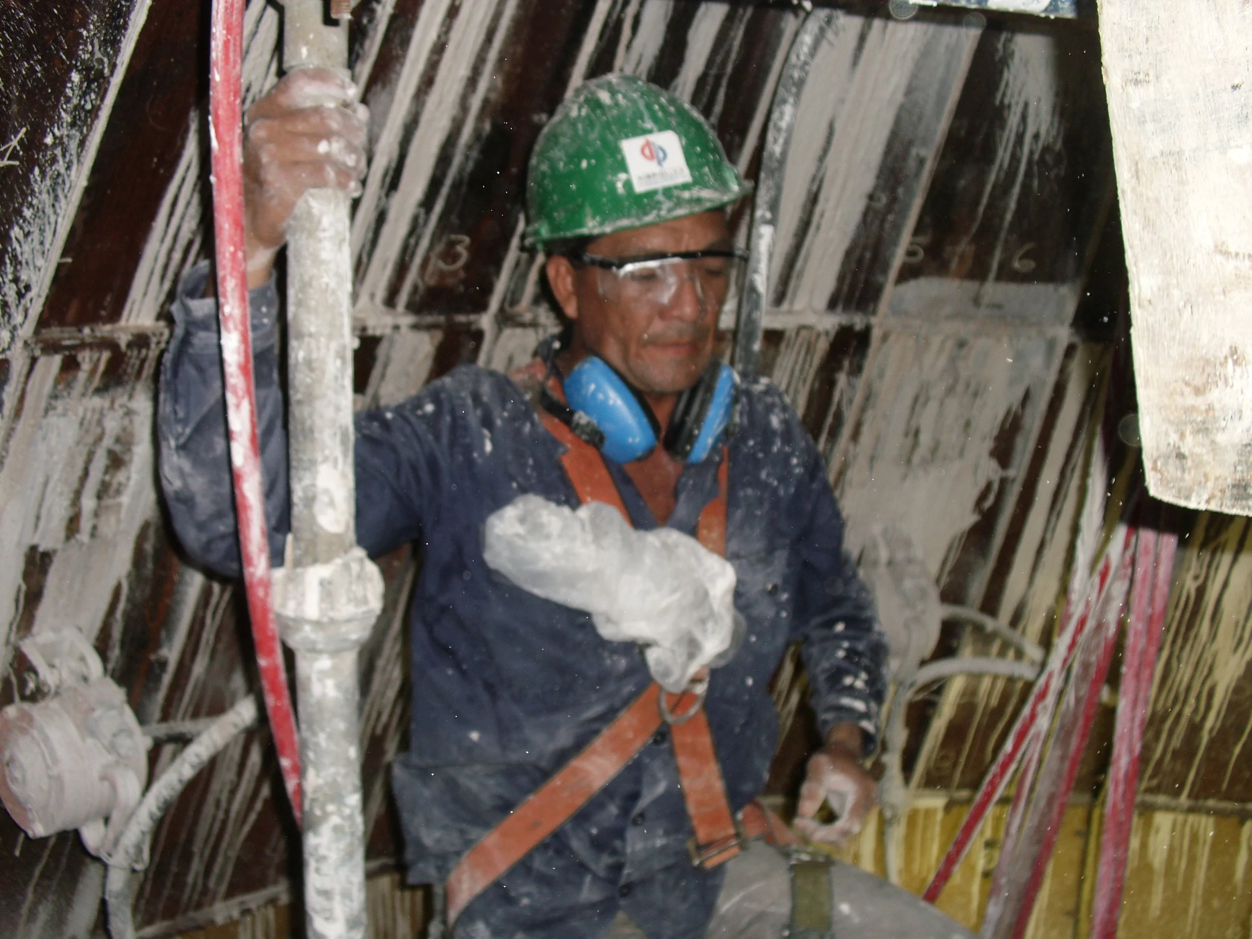 vaciado de reformador secundario. Trabajadores en uniformes y cascos de seguridad mezclando material refractario en una estructura de andamios durante la noche.