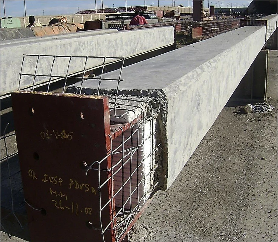 viga de concreto en un sitio de construcción con refuerzo de acero en un extremo y letras en español en un bloque de metal}