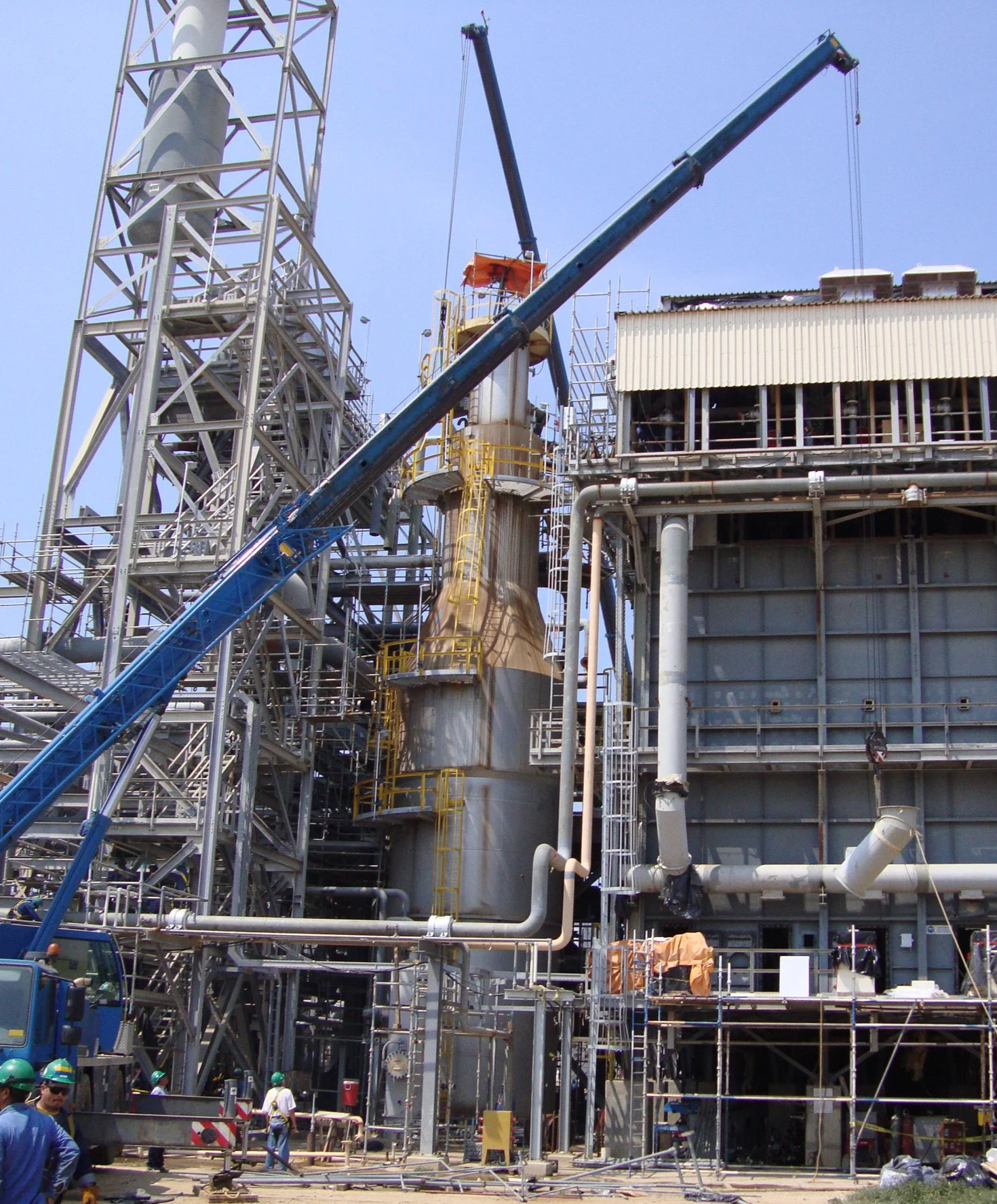 Construcción planta  industrial con estructura metálica, maquinaria y algunos trabajadores con casco en un sitio de construcción.