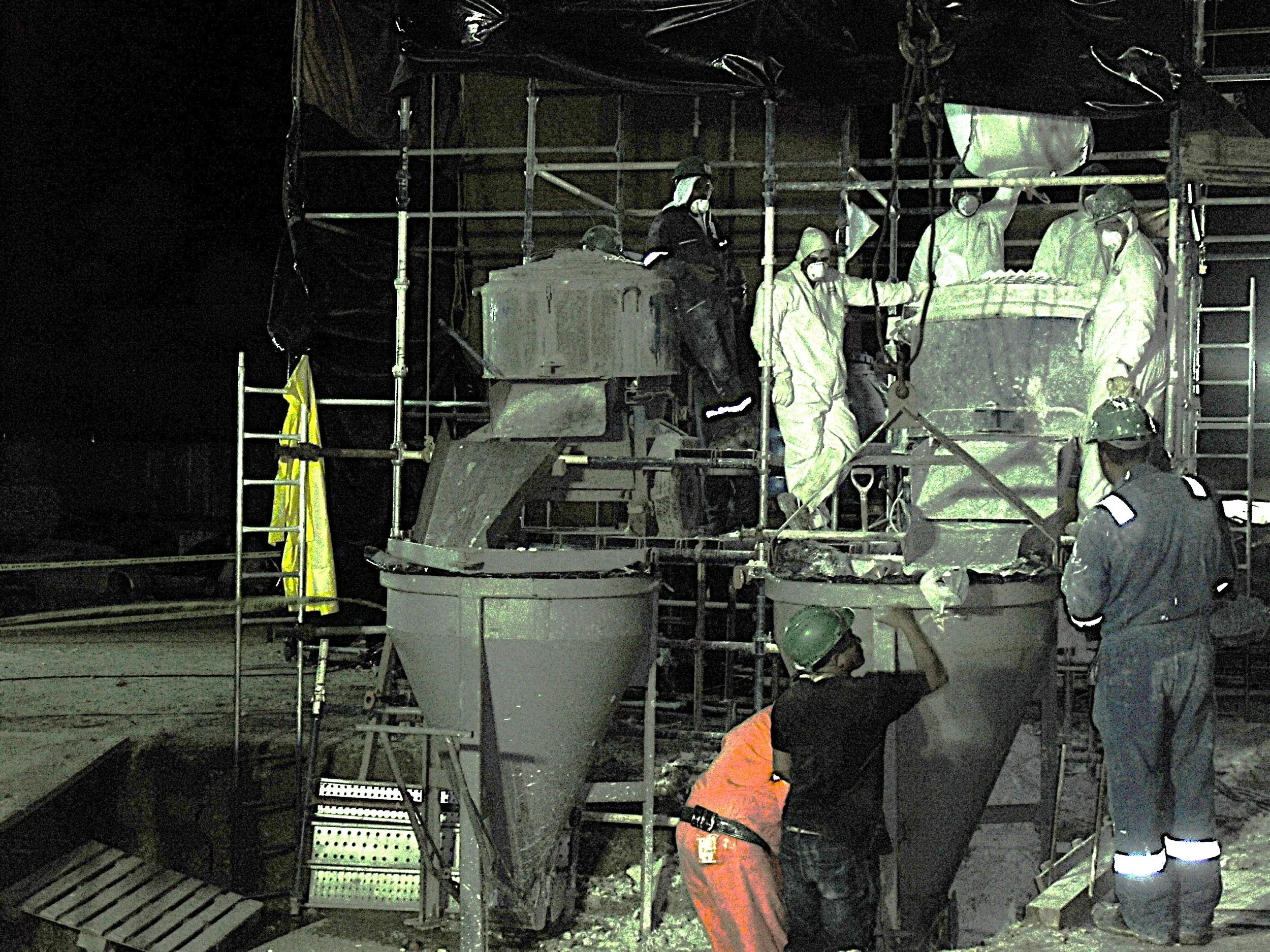 vaciado de reformador secundario. Trabajadores en uniformes y cascos de seguridad mezclando material refractario en una estructura de andamios durante la noche.