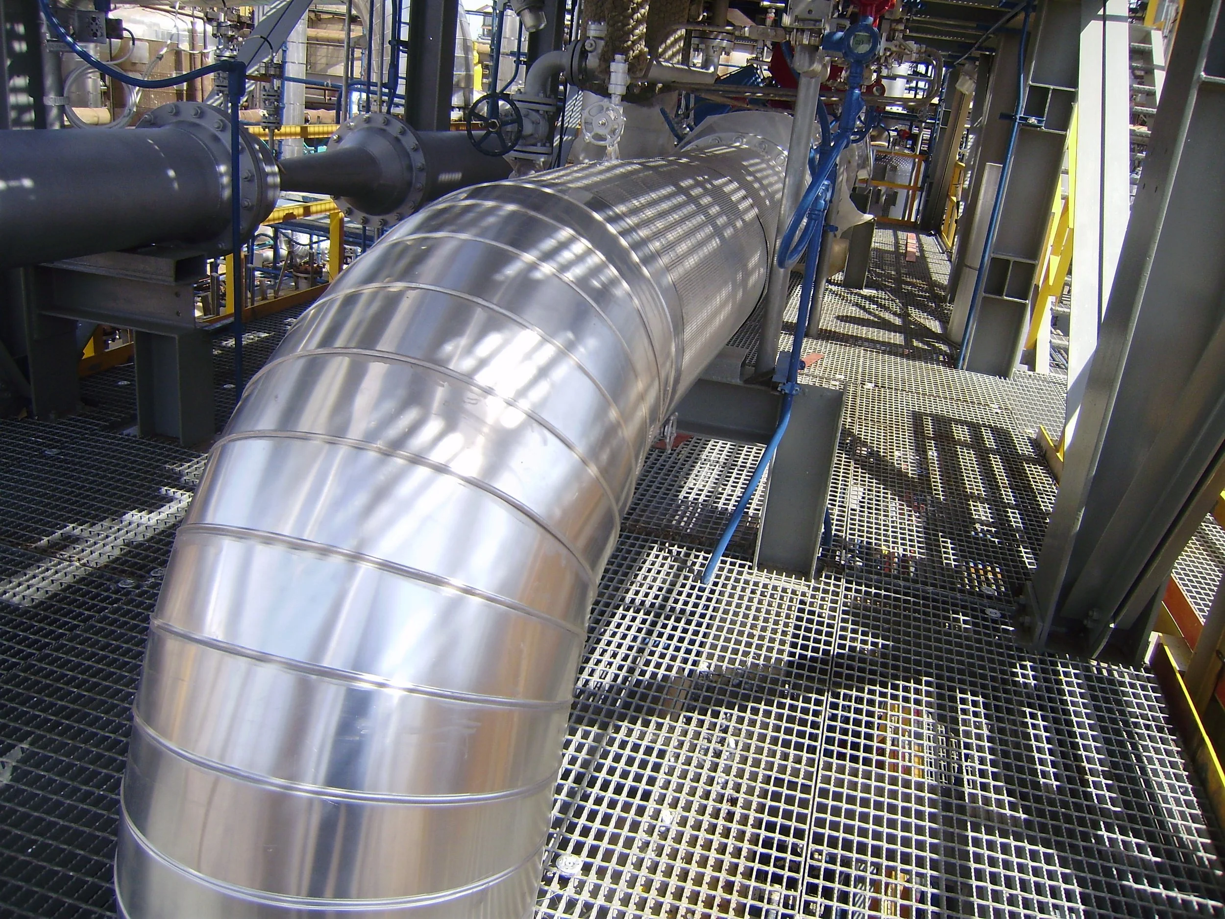 Vista de una tubería metálica grande en una planta industrial con estructura de rejillas de metal y otros componentes de maquinaria.