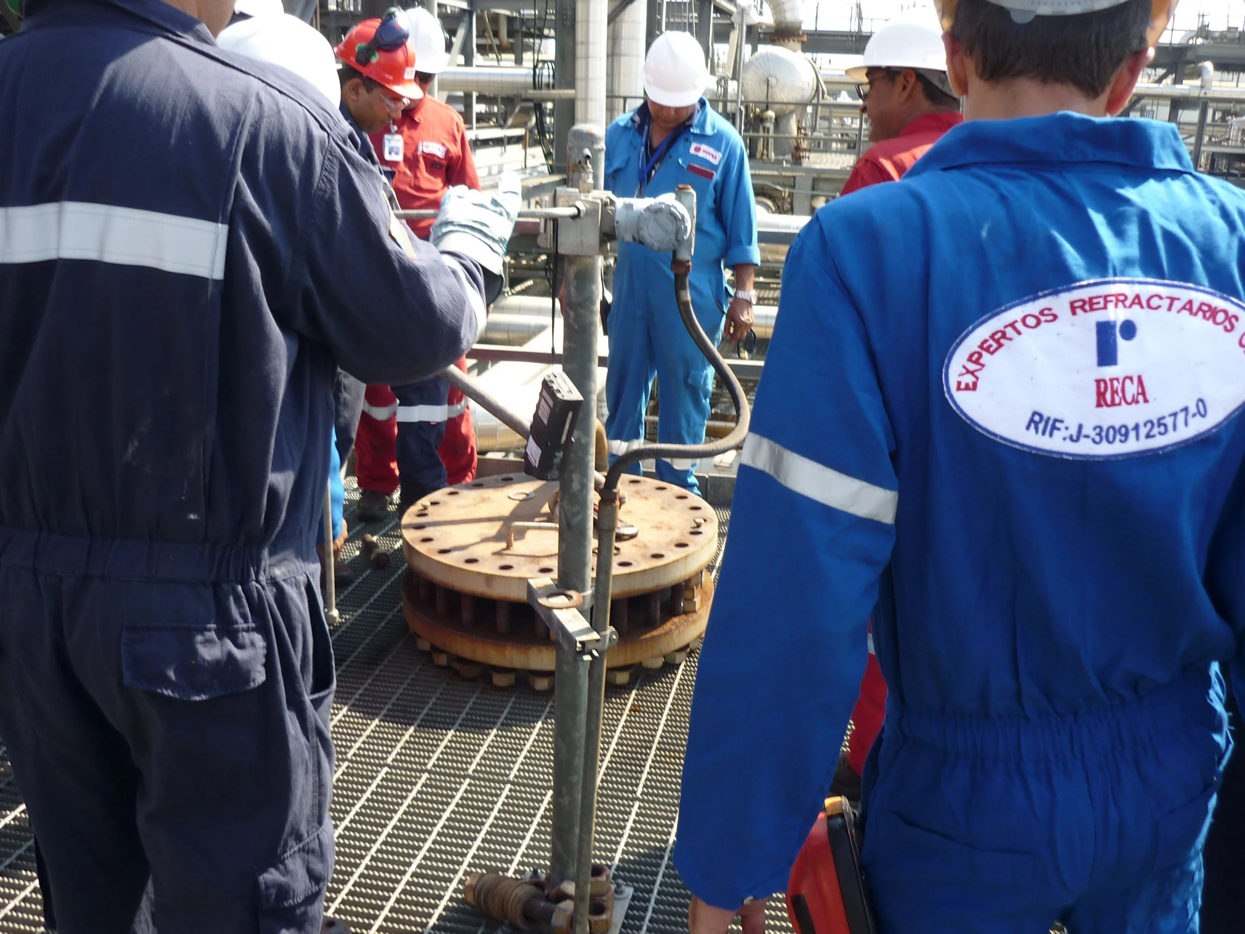 Grupo de ingenieros y técnicos en uniforme de trabajo inspeccionando un equipo industrial en una plataforma de petróleo o una planta de procesos.