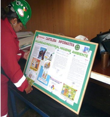 Persona revisando un cartel informativo sobre seguridad industrial, higiene y ambiente, en un entorno interior.