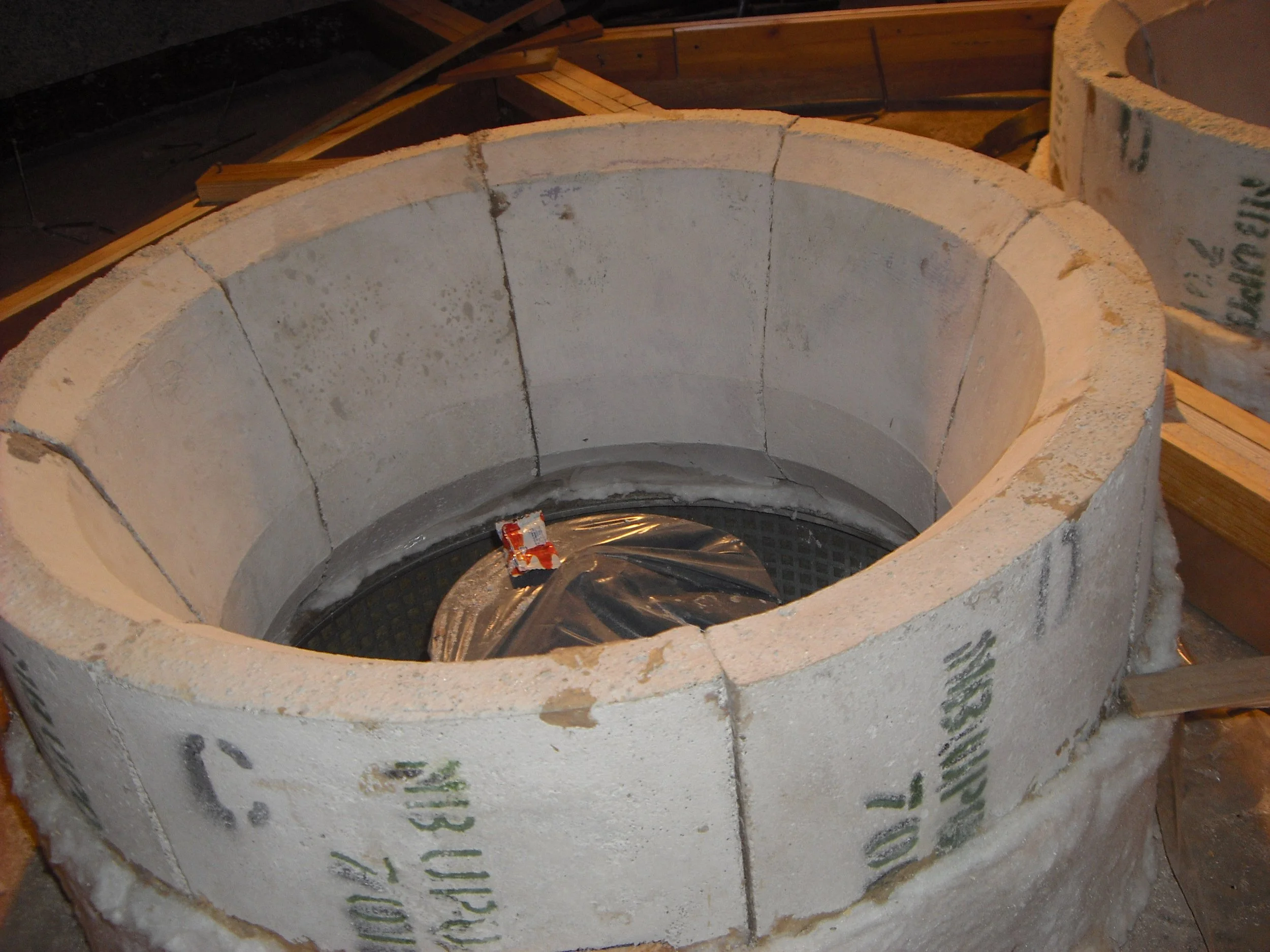 Horno de ladrillo en construcción, rodeado de madera en un entorno de obra.
