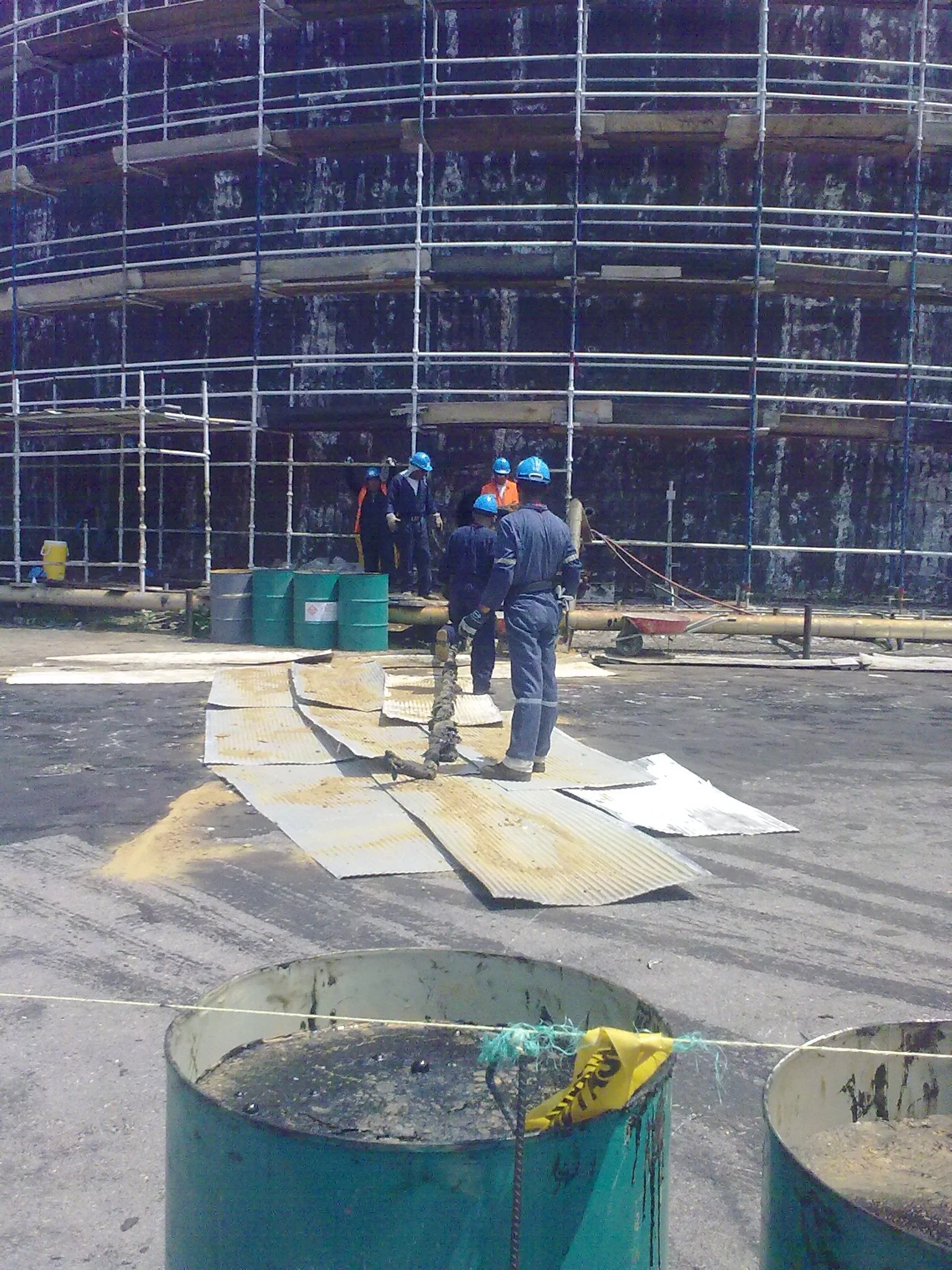 Rehabilitacion. Trabajadores con casco en una estructura de andamios alrededor de tanque de almacenamiento petrolero