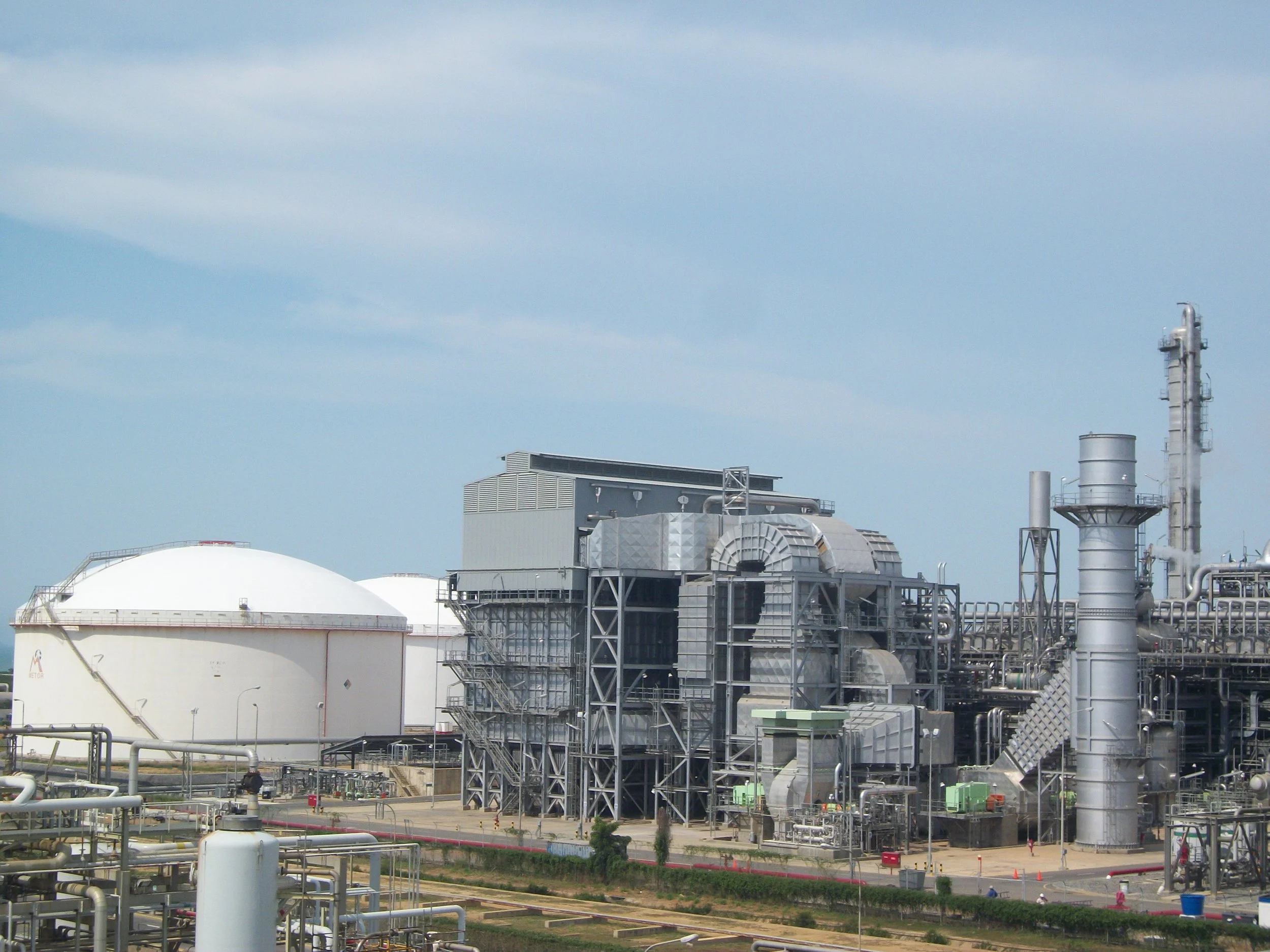 Planta industrial con tanques grandes y estructuras metálicas, cielo despejado.