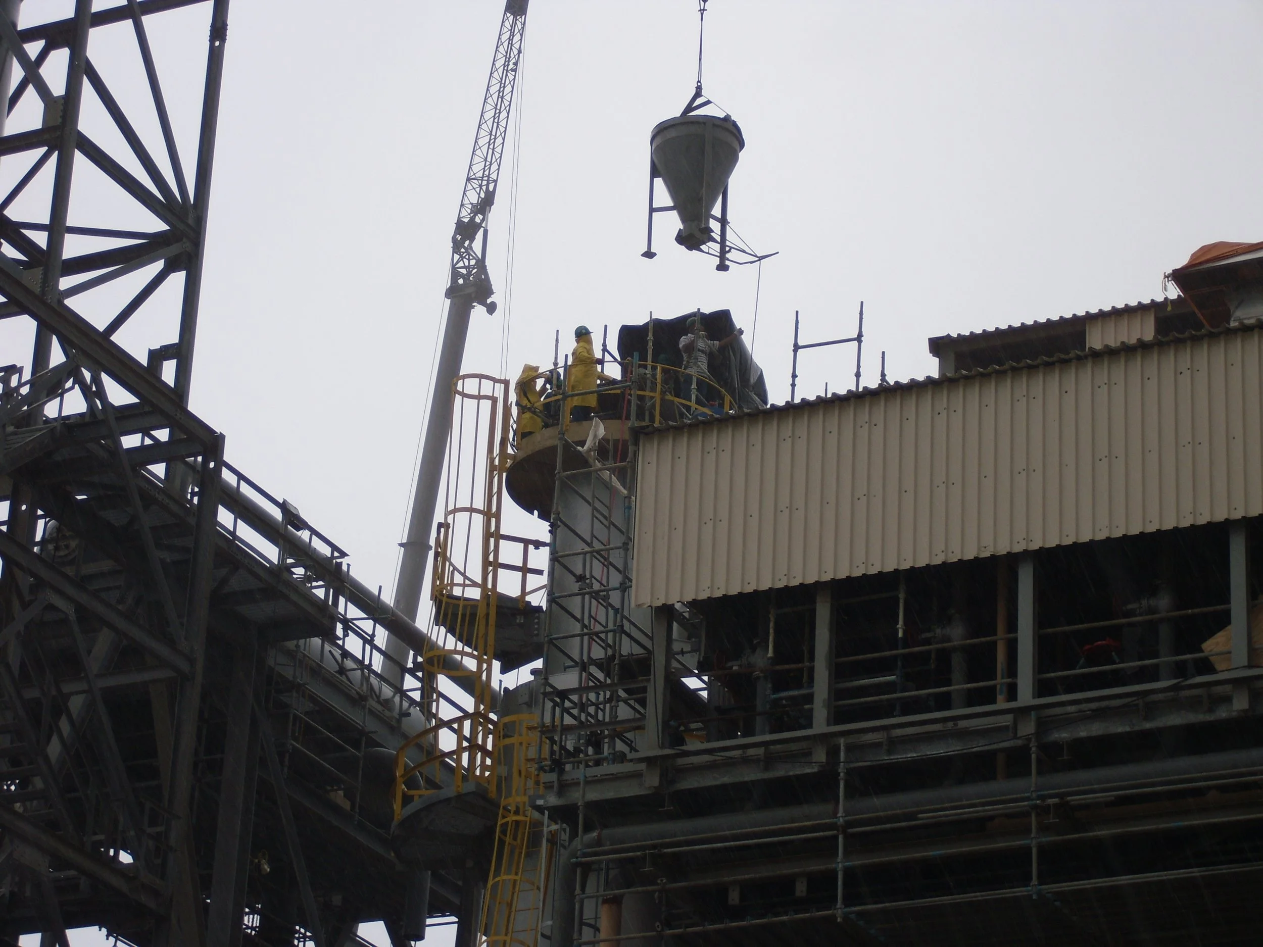 Trabajadores en una construcción de estructura metálica con una grúa levantando material refractario