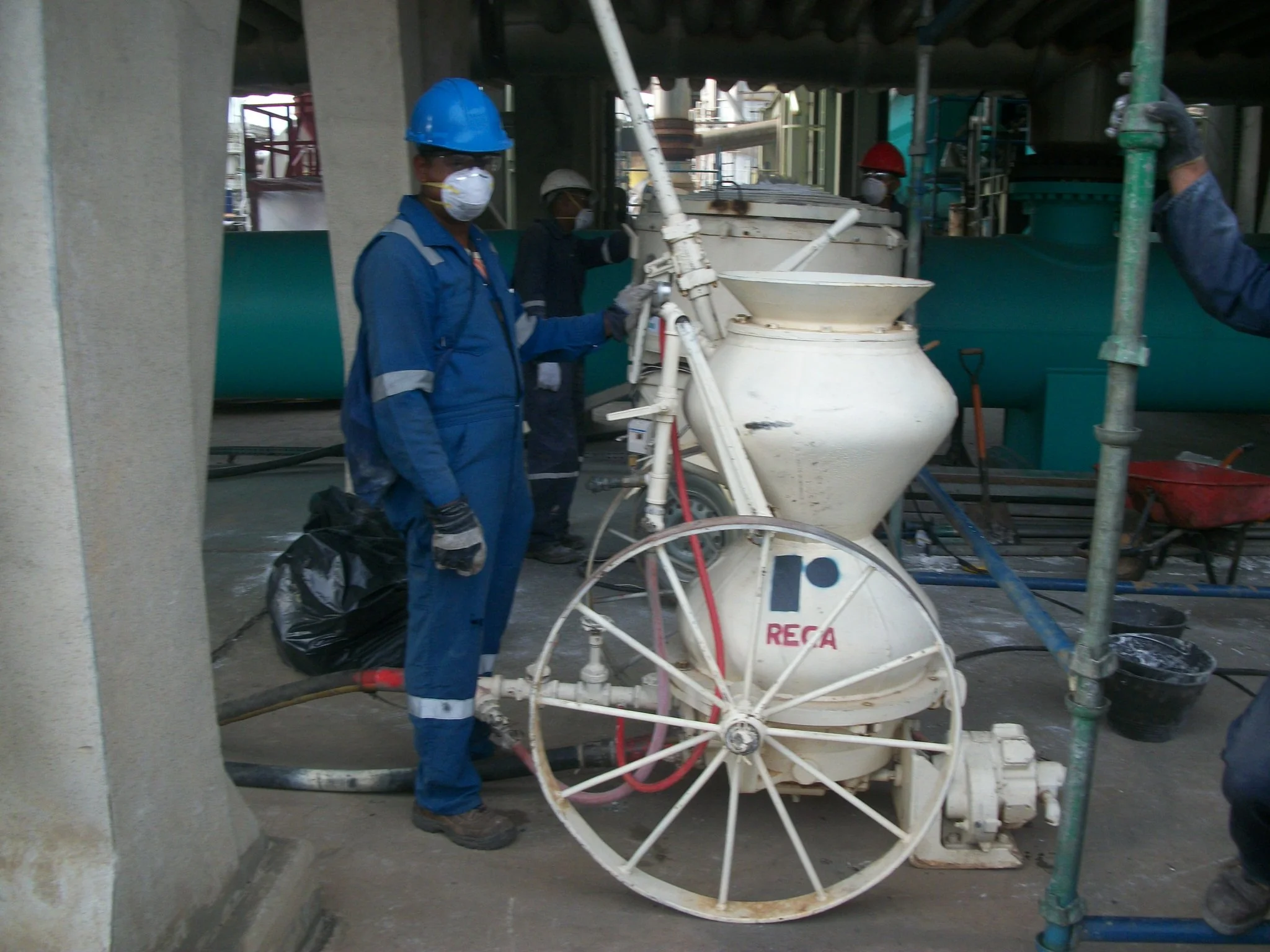 Personal de construcción operando una máquina proyectadora de concreto en una obra de construcción, con casco y mascarilla.