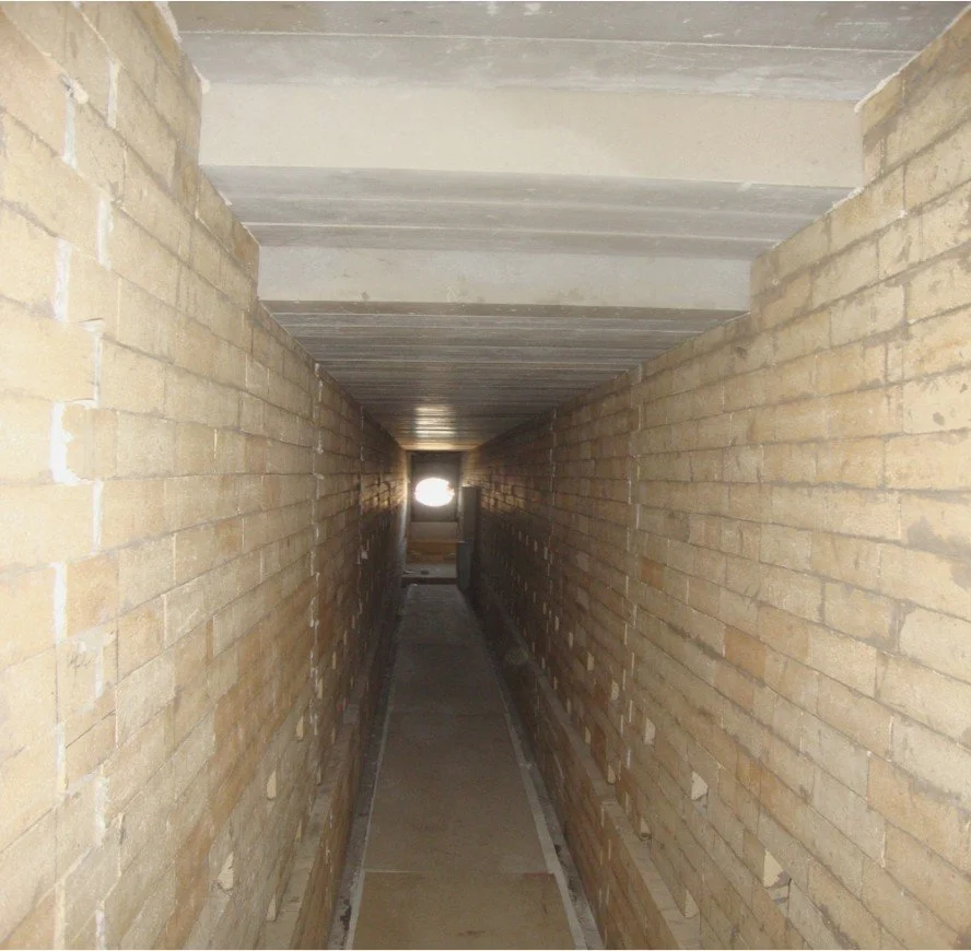 Tunel con paredes de ladrillo y techo de concreto refractario, con luz natural en el fondo.