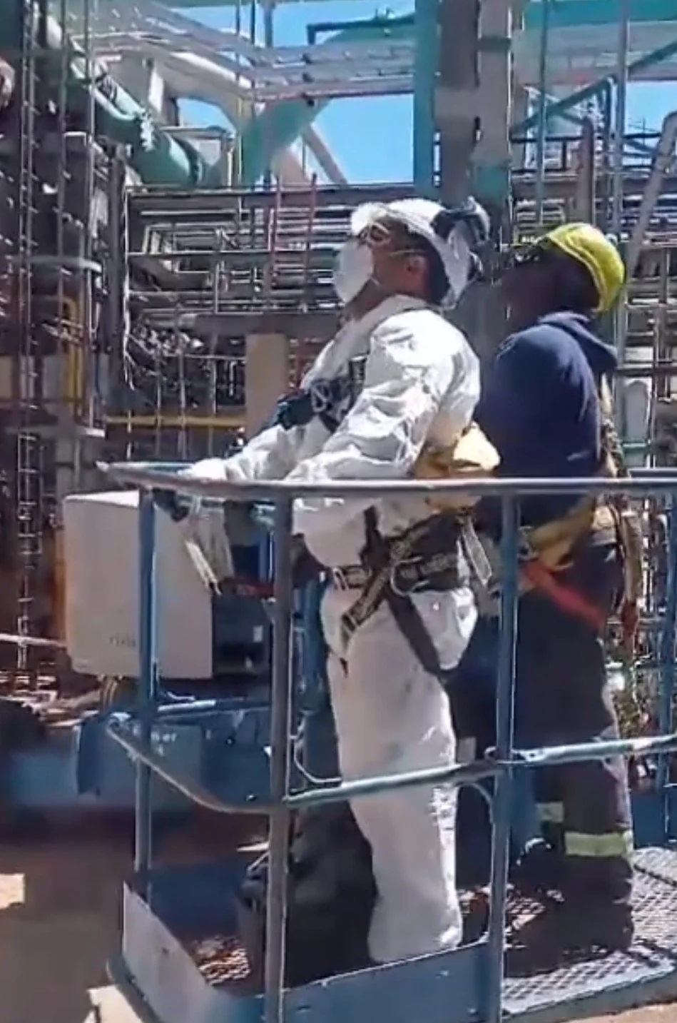 Persona en protección de equipo de protección personal (EPP) en un entorno industrial con estructuras metálicas y tuberías.