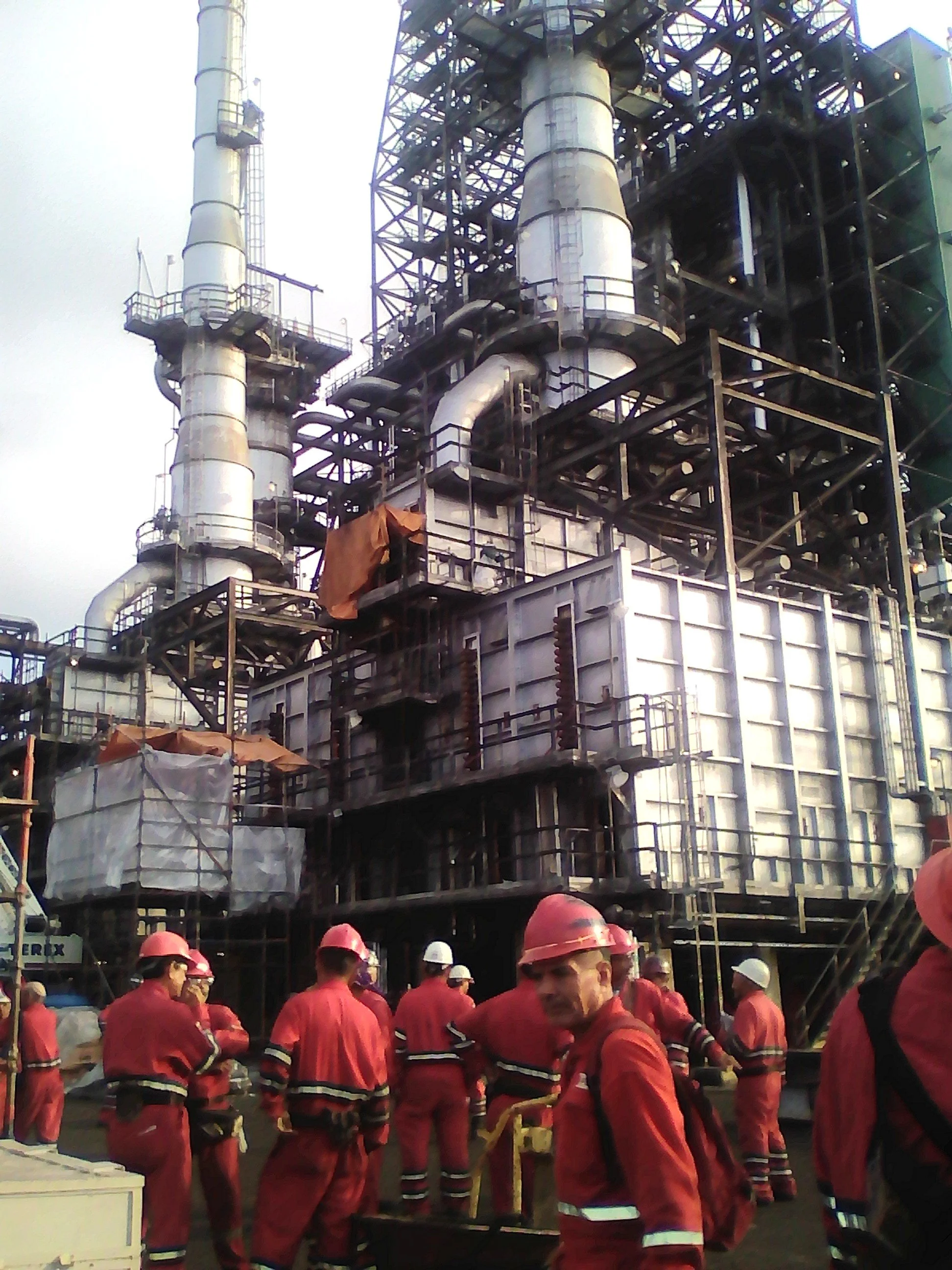 Trabajadores en uniforme rojo y cascos rojos operan maquinaria en una refineria.