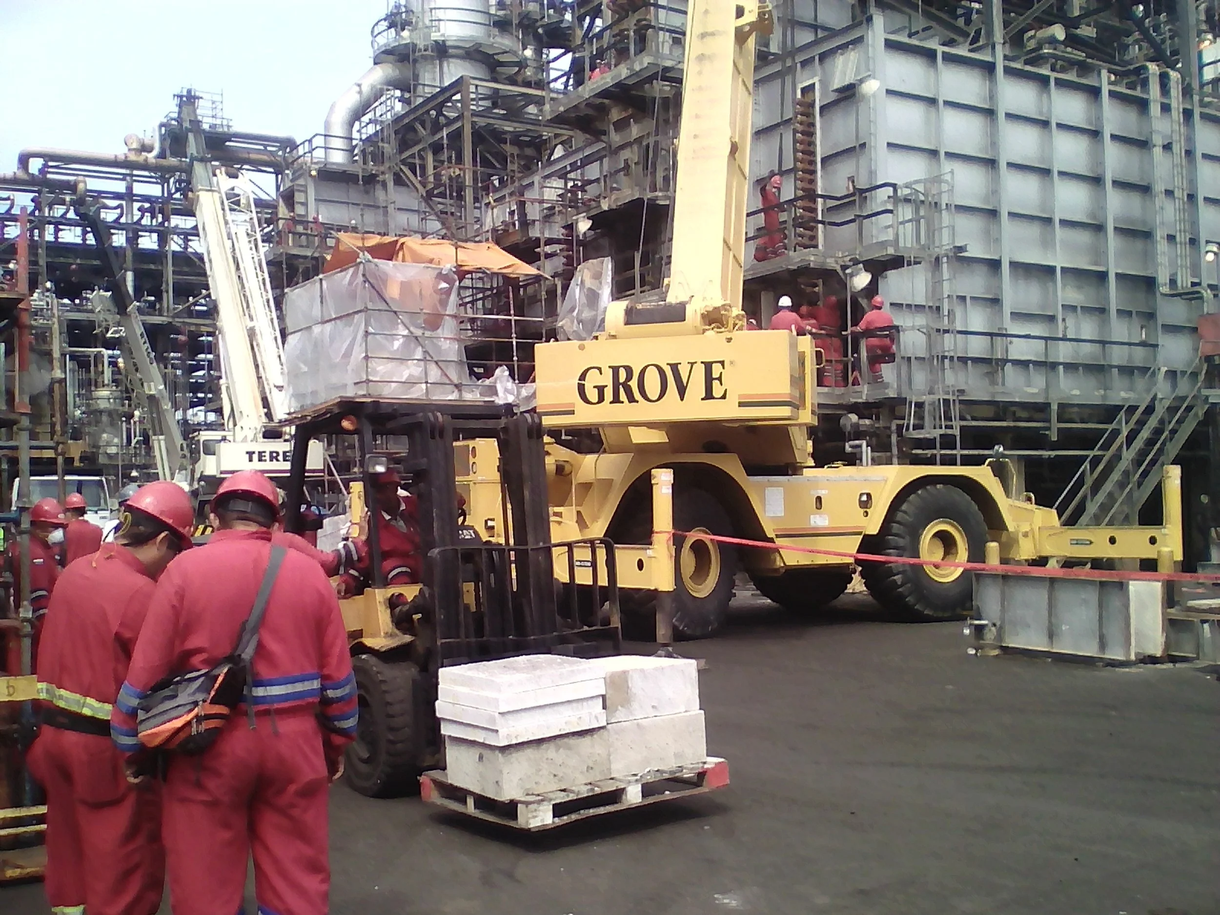 Trabajadores en uniforme rojo y cascos rojos operan maquinaria en una refineria.