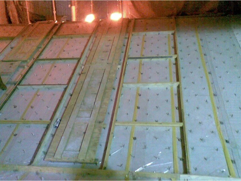 Estructura de madera en construcción, vista del interior de un techo o piso, con paneles aislantes y maderas enmarcadas.