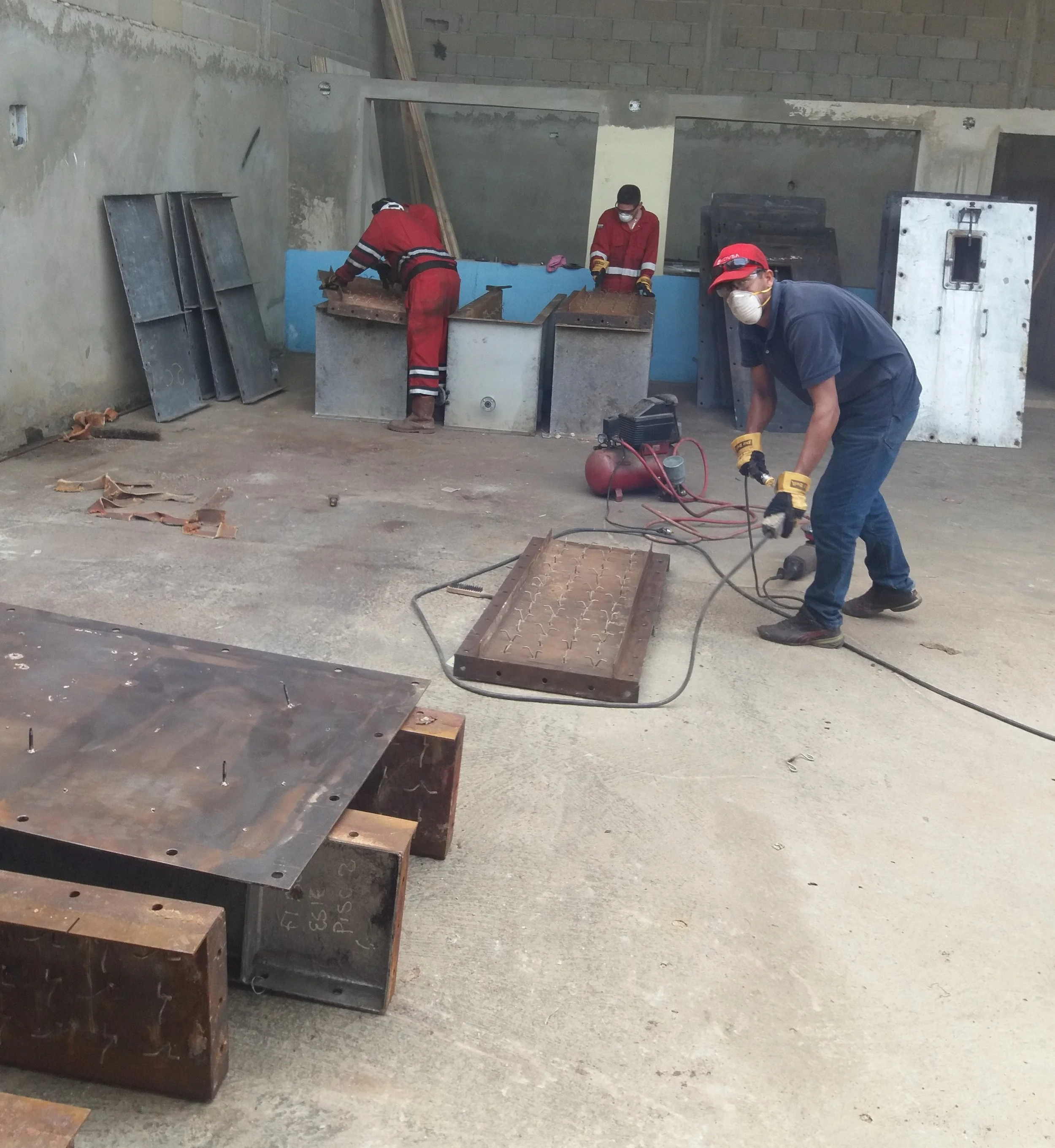 Personas trabajando en la fabricación o ensamble de estructuras metálicas en un taller de metalurgia, usando equipo de protección personal y herramientas eléctricas.
